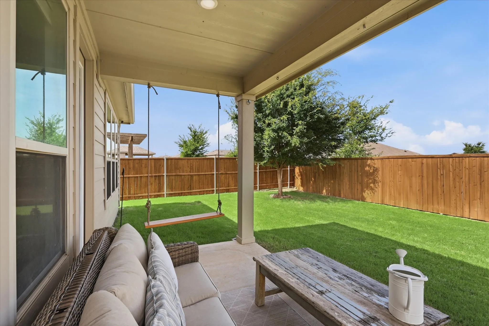 Covered patio with a tile floor, offering direct access to a fenced backyard featuring a manicured lawn and mature trees