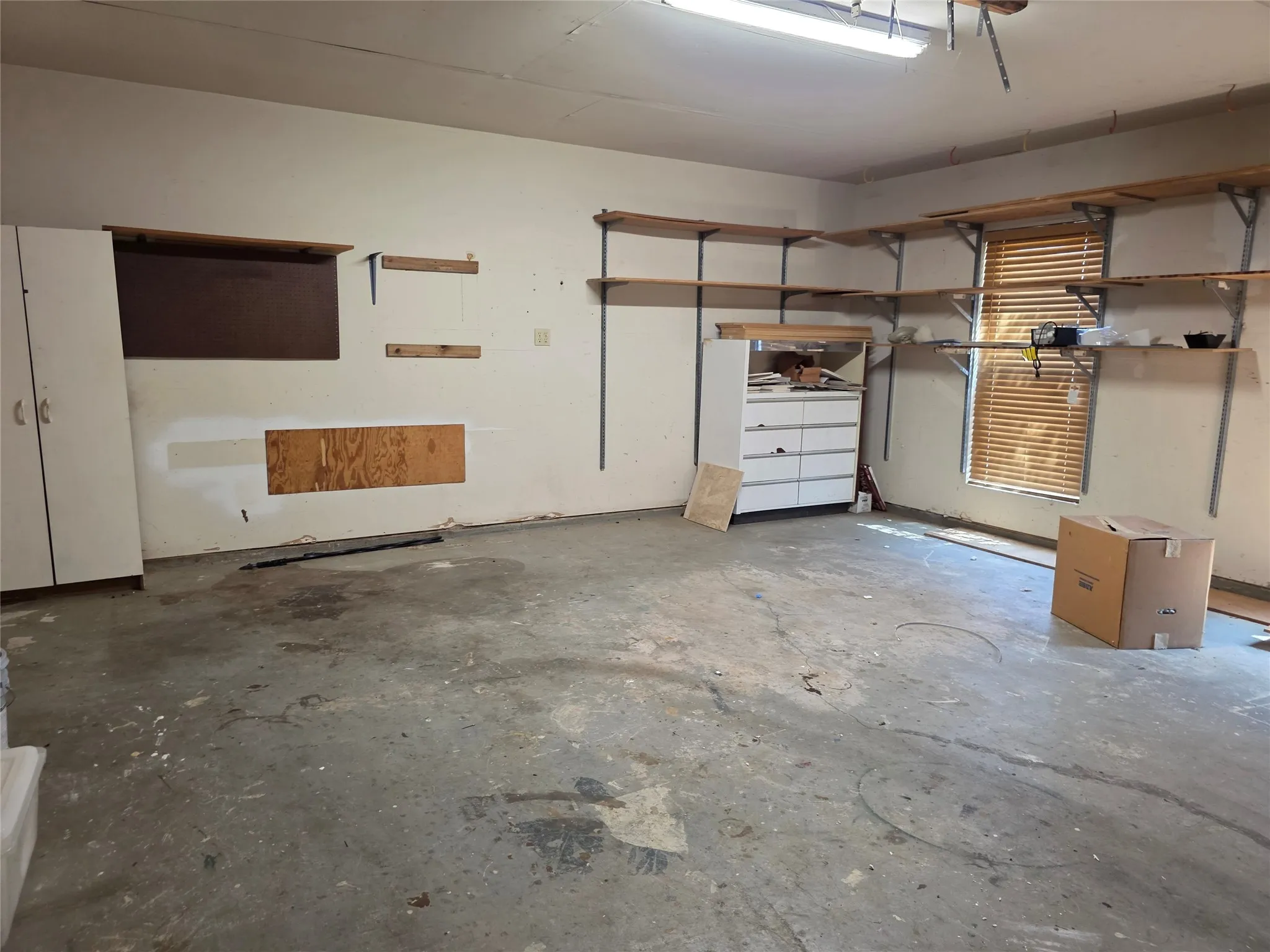 Garage space featuring built-in shelving, concrete flooring, and a window with blinds
