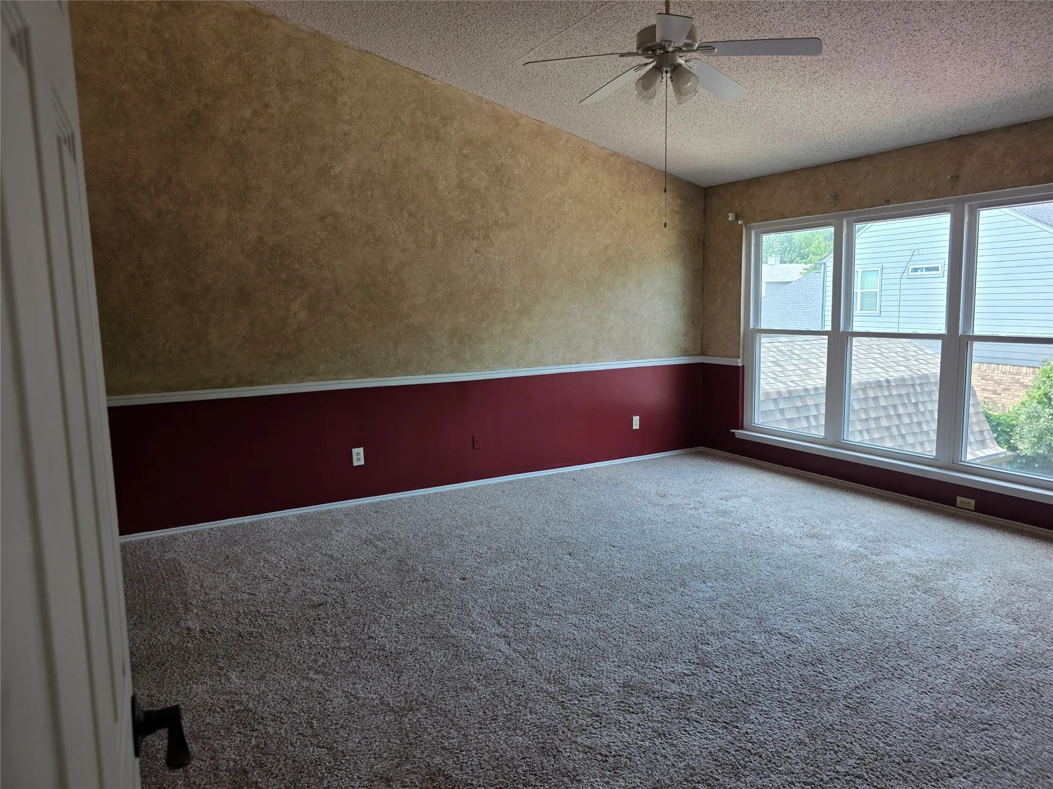 Spacious room featuring vaulted ceilings, a ceiling fan, plush carpeting, a large window array, and two-tone wall finishes with chair rail molding