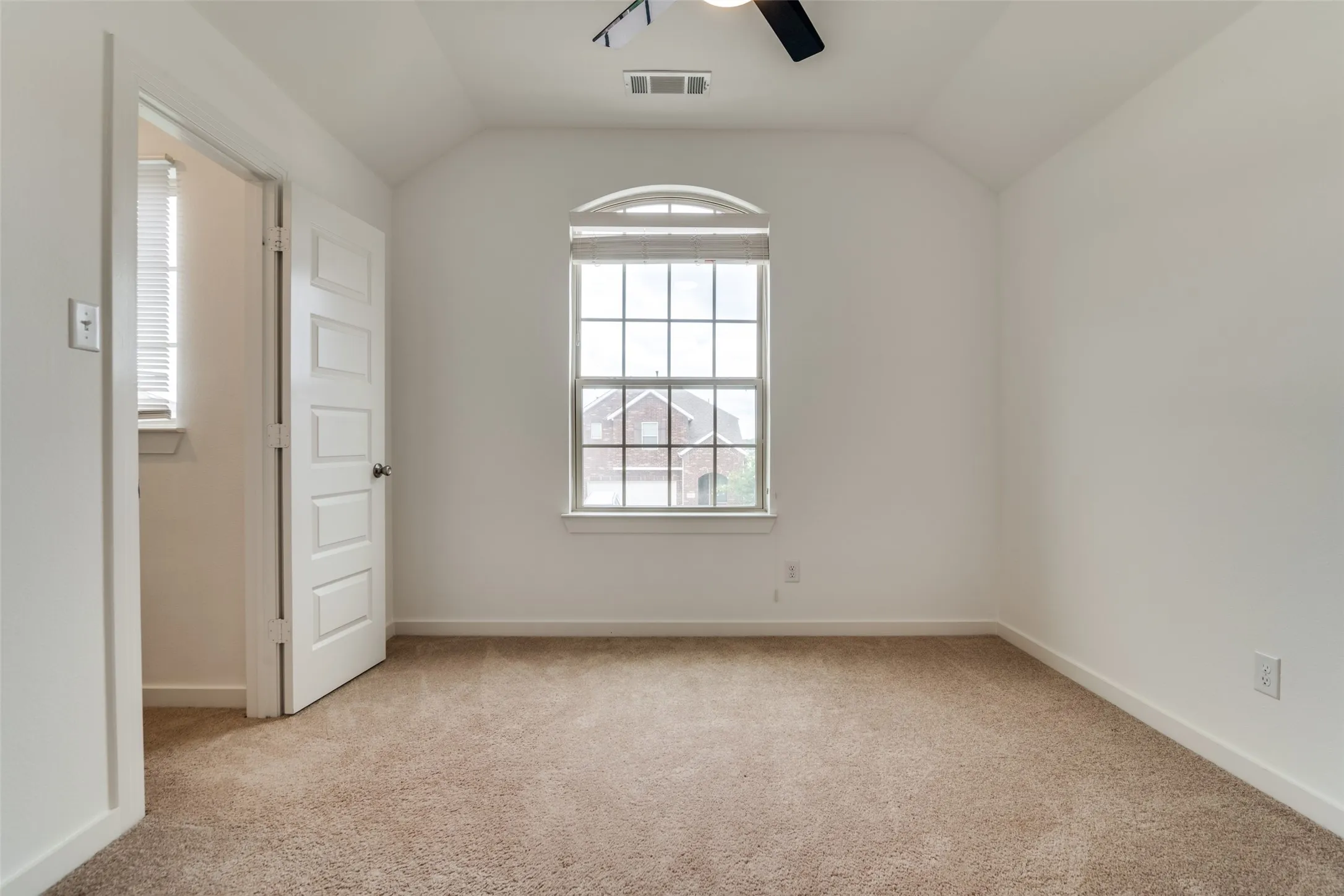 Carpeted room featuring an arched window, white paneled door, and a ceiling fan