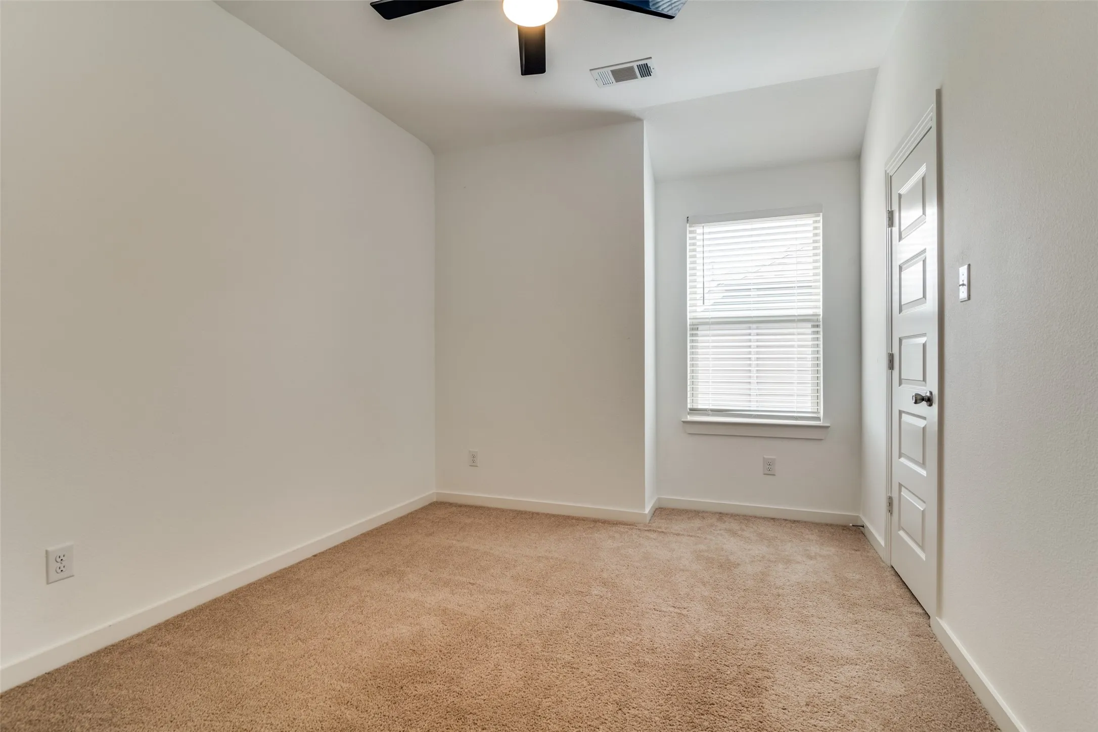 Bright room featuring neutral-toned carpet, white walls, and a window with blinds