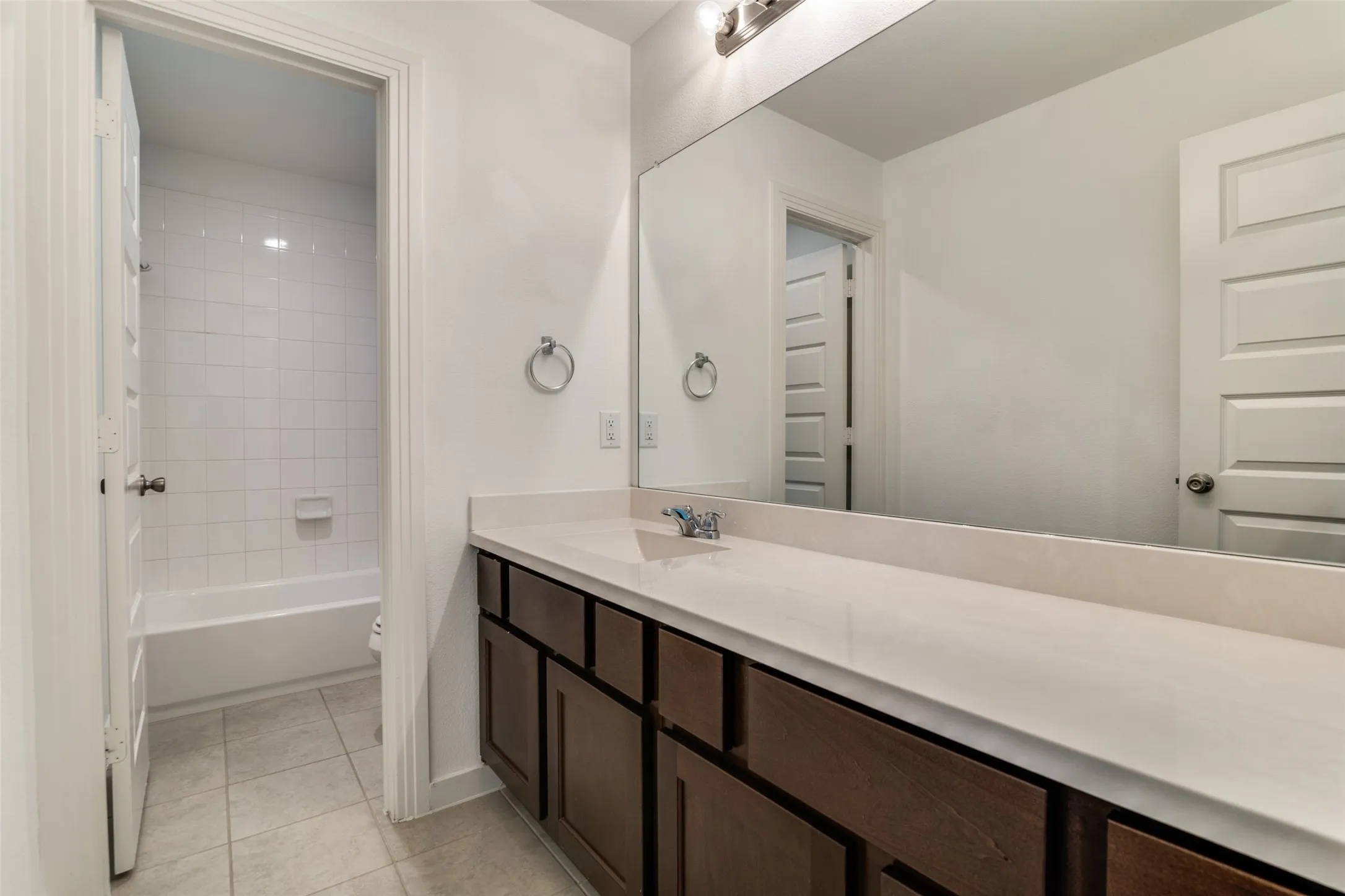 Bathroom featuring a spacious vanity with an undermount sink, a light-toned countertop, and dark wood cabinetry