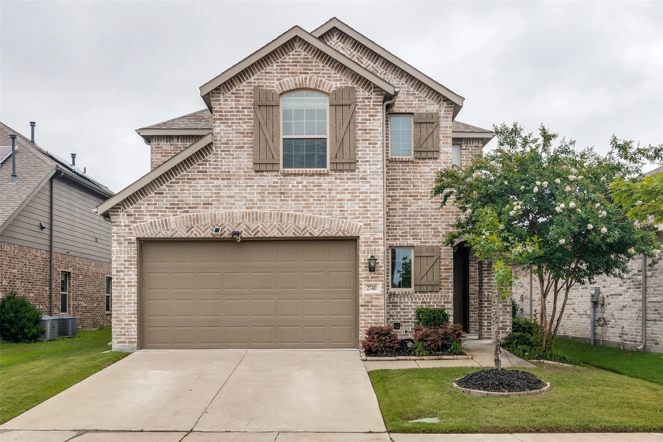 Brick facade featuring decorative shutters, a two-car garage, and landscaped front yard