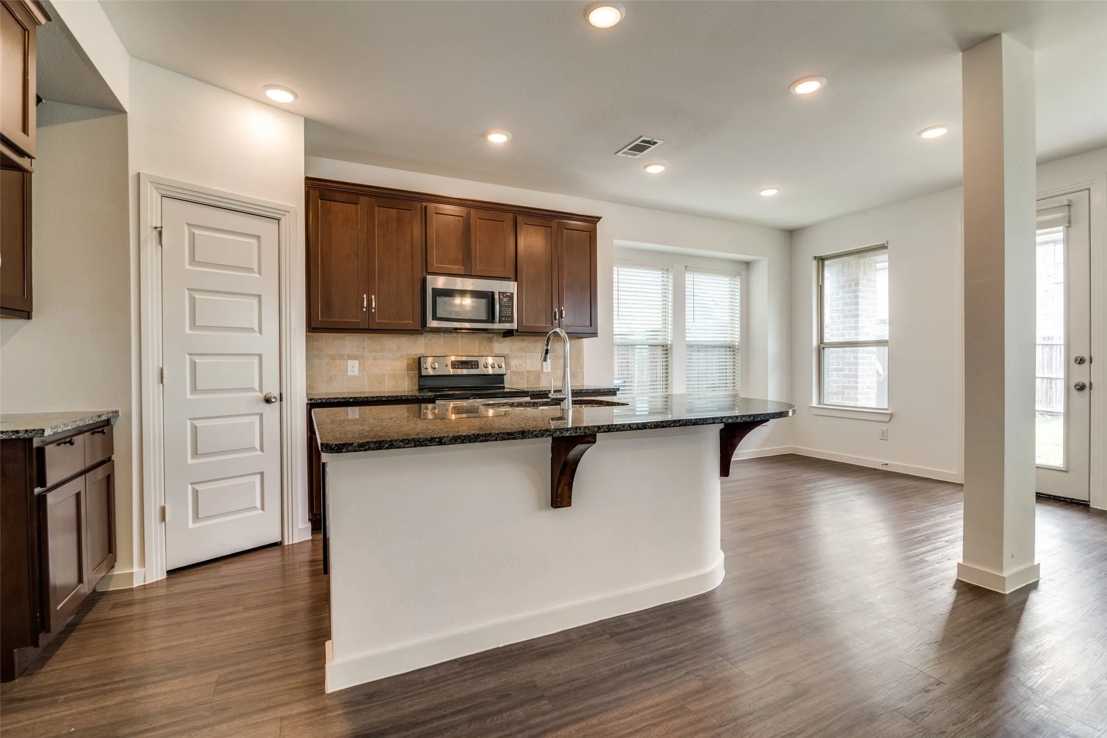 Kitchen featuring dark wood cabinetry, stainless steel appliances, a tiled backsplash, and a breakfast bar with a granite-style countertop