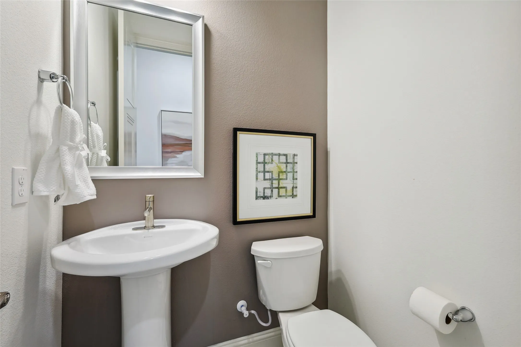 Pedestal sink with polished chrome faucet, framed mirror, and two-tone wall finishes
