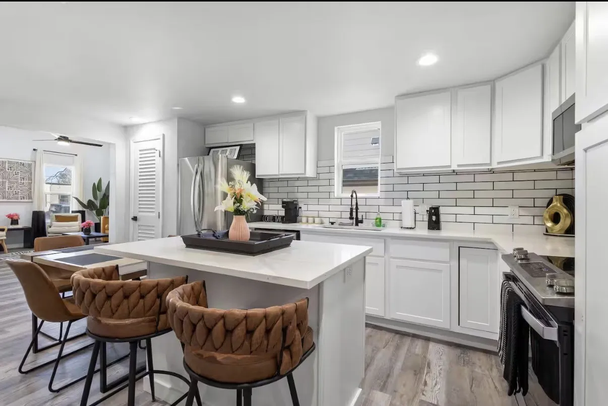 Contemporary kitchen featuring an island with a light-toned countertop, white cabinetry, a subway tile backsplash, stainless steel appliances, and wood-finish flooring