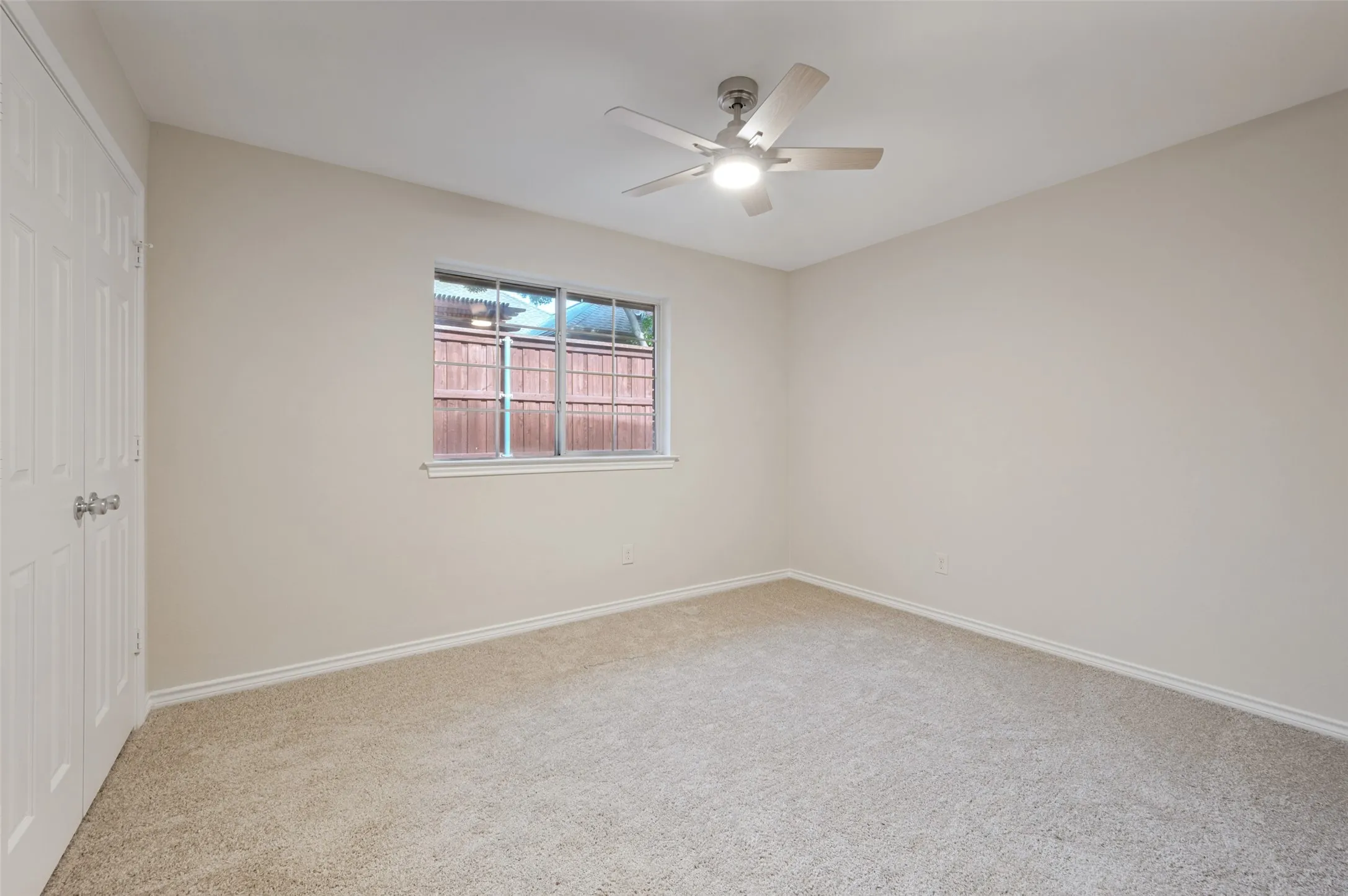 Carpeted room featuring a ceiling fan with integrated lighting, a window with a white frame, and a paneled bifold closet door