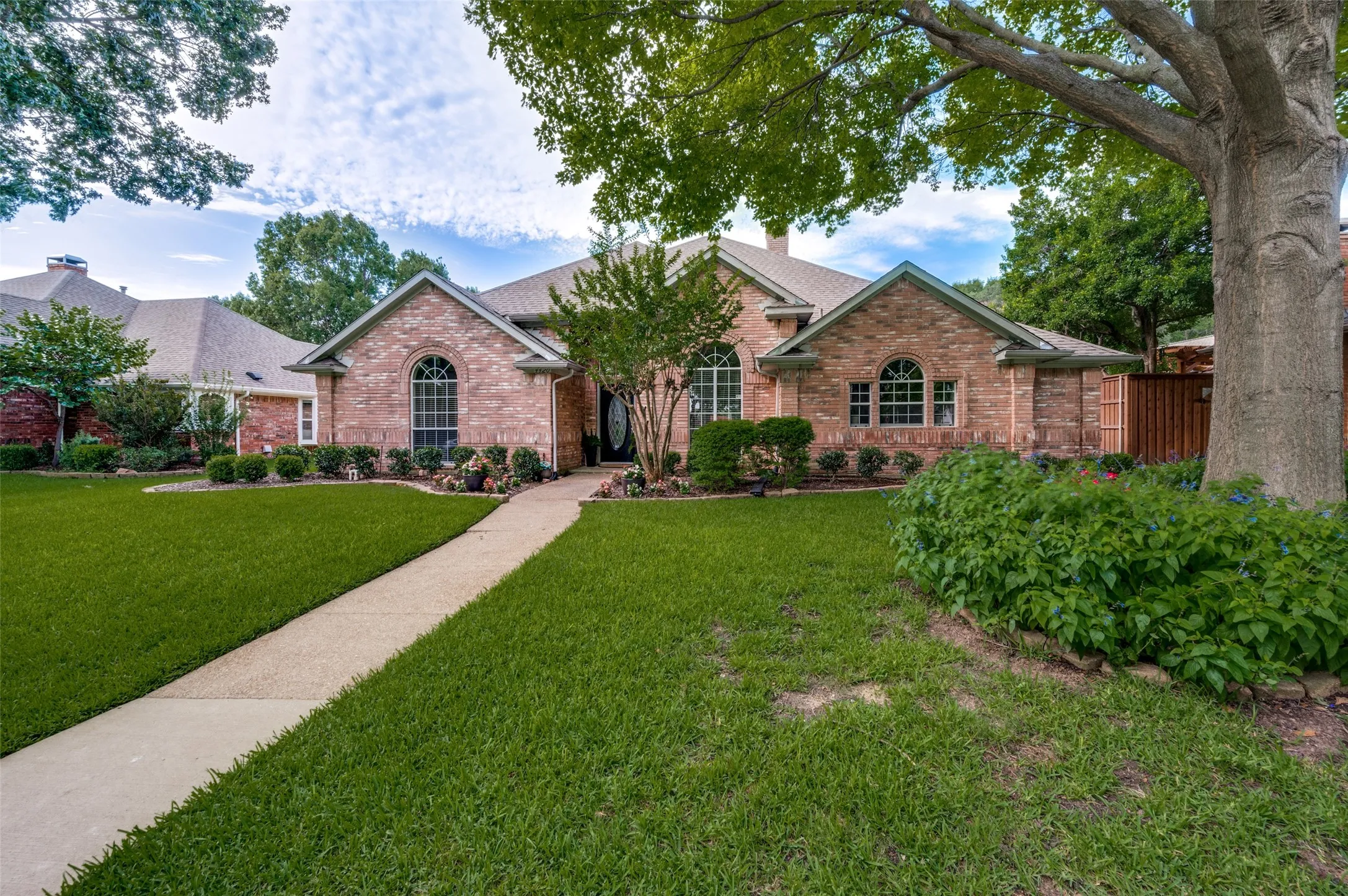 Established trees and landscaping frame this front entry with arched windows, and a concrete pathway