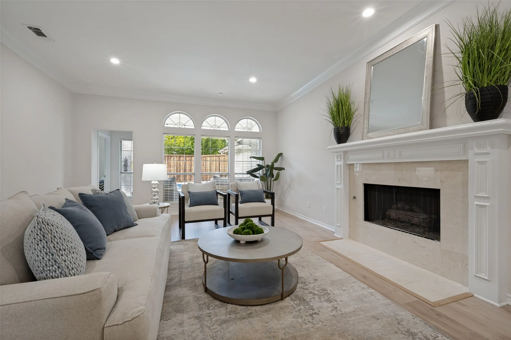 Living area featuring a classic fireplace with a stone surround and hearth, bright recessed lighting, wood-finish flooring, and multiple arched windows