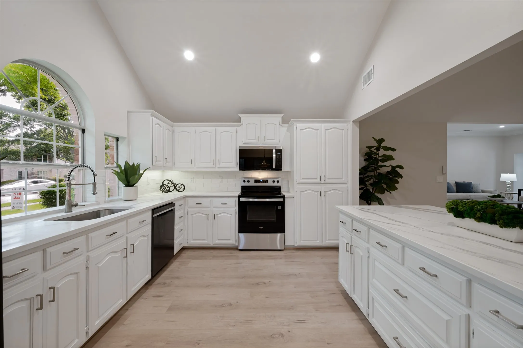Kitchen featuring high vaulted ceilings, white cabinetry with silver hardware, a large arched window, and wood-finish flooring