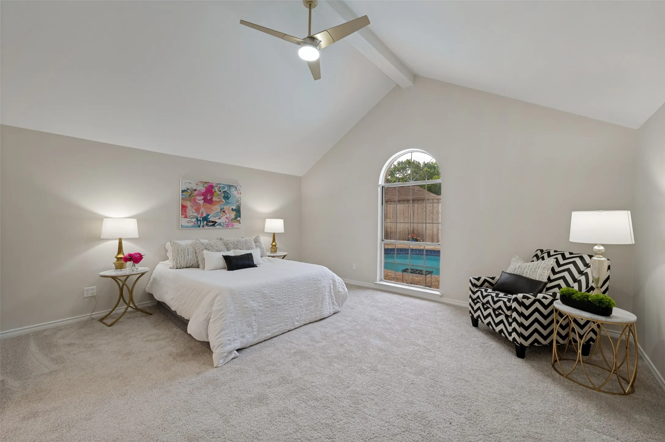 Spacious room featuring vaulted ceilings with an exposed beam, a ceiling fan, a large arched window, and light-toned carpeting