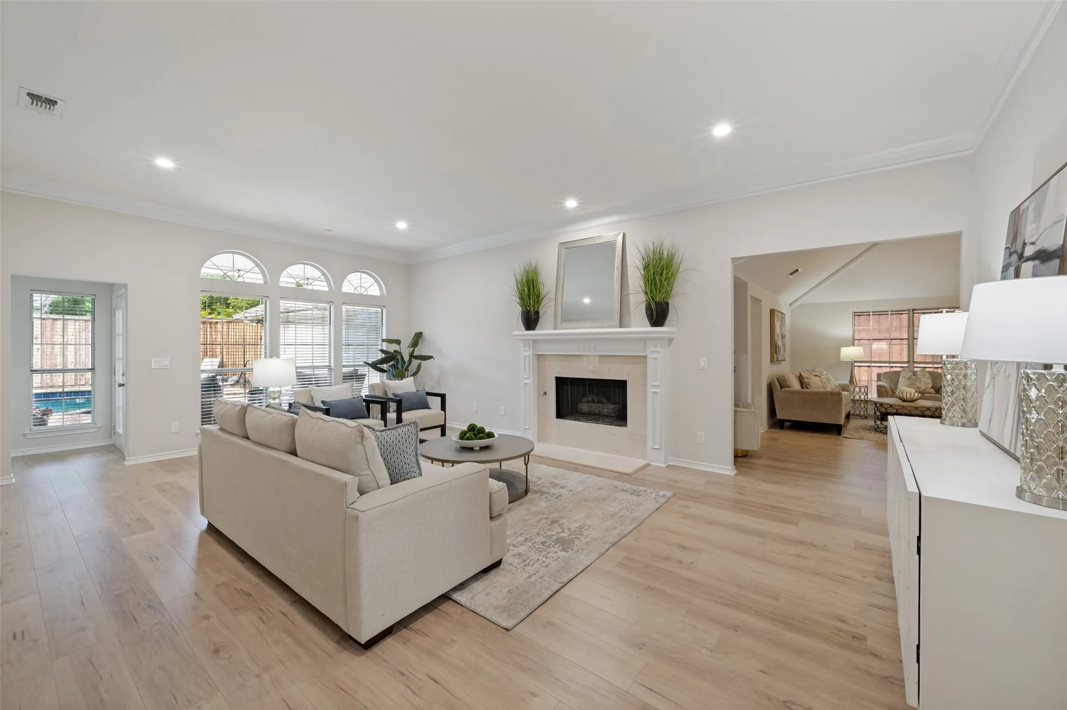 Spacious living area featuring light wood-finish flooring, a stone-surround fireplace with a white mantel, recessed lighting, and crown molding