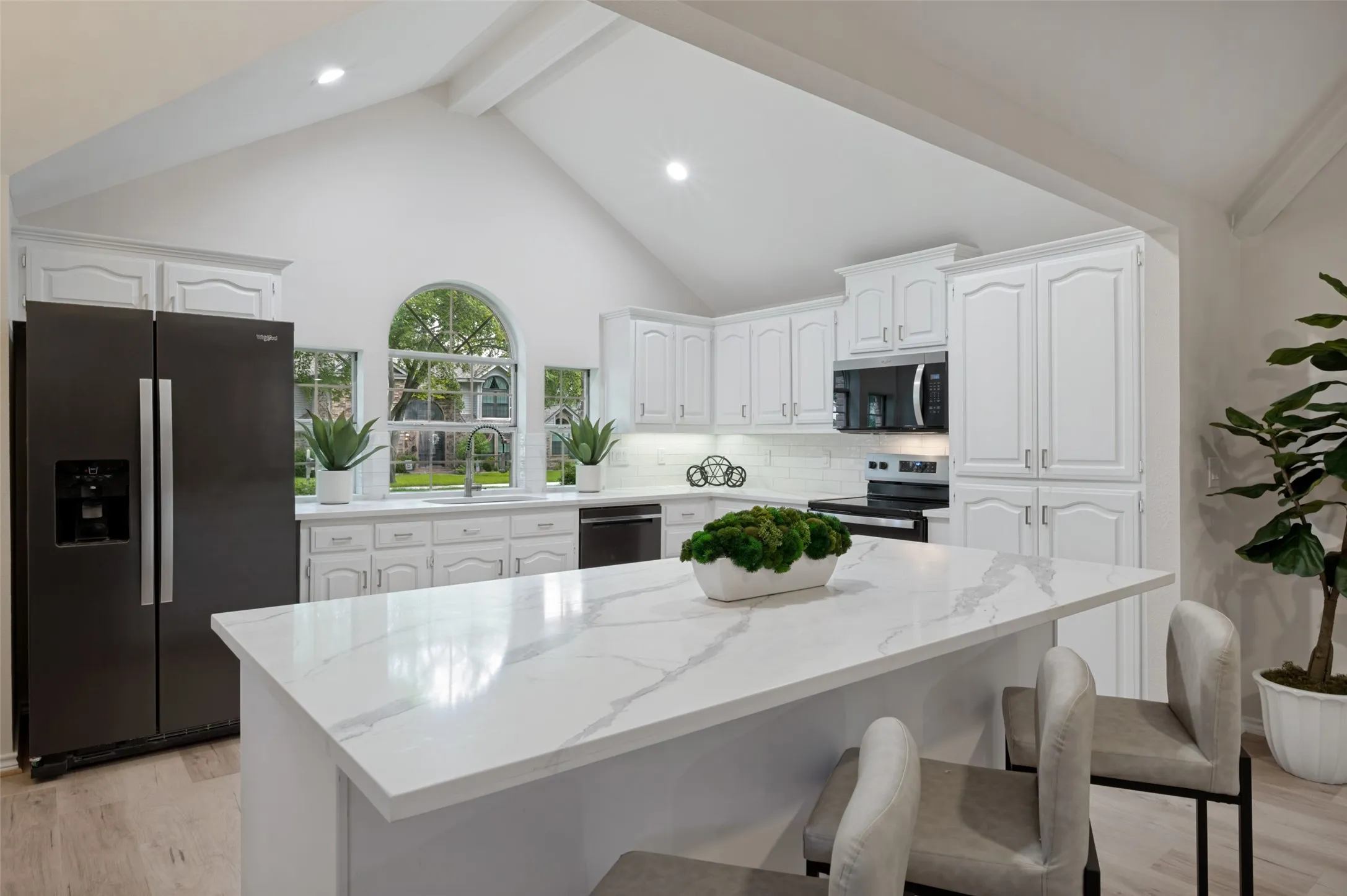 Kitchen featuring a central island with a stone-finish countertop, white cabinetry, vaulted ceilings, and an arched window above the sink