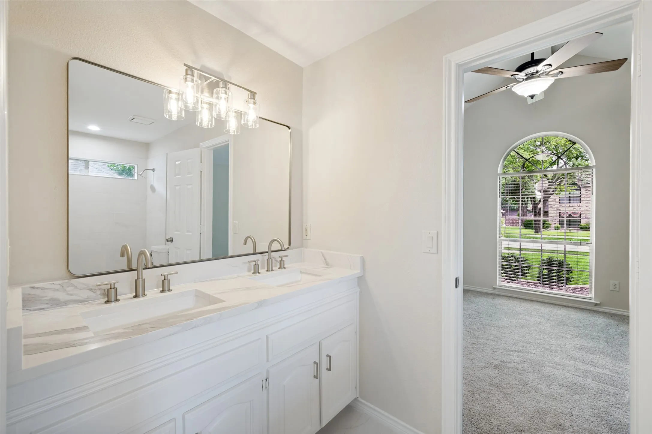 Double vanity with integrated sinks and brushed nickel fixtures, complemented by a rectangular mirror with a metal frame and a five-light vanity fixture