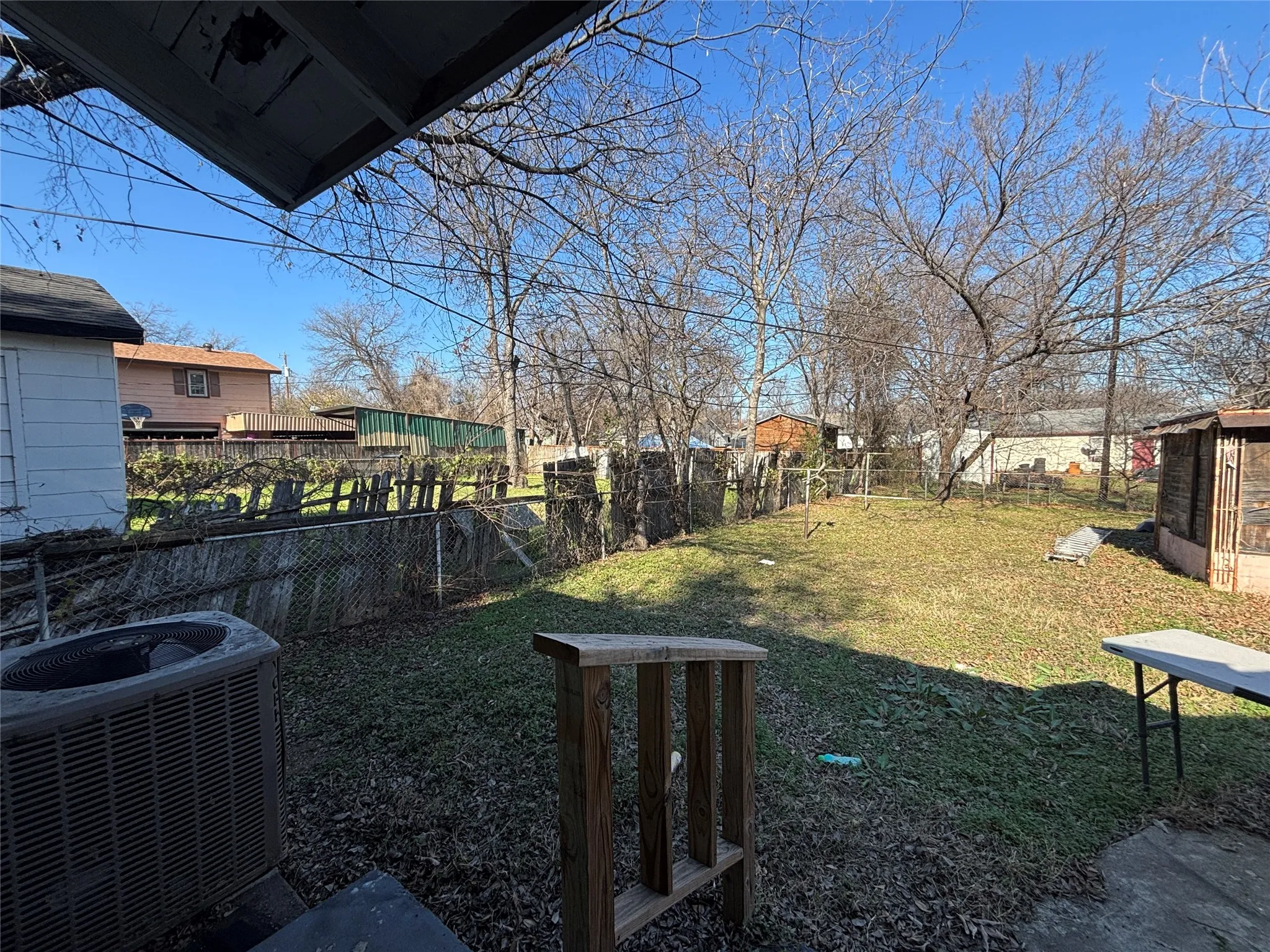 Expansive backyard featuring a partial chain-link fence, mature trees, and a ground-level concrete patio