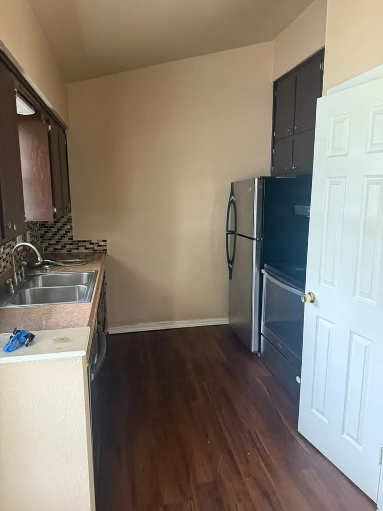 Kitchen featuring wood-finish flooring, dark wood cabinetry, a double basin stainless steel sink, and a patterned tile backsplash