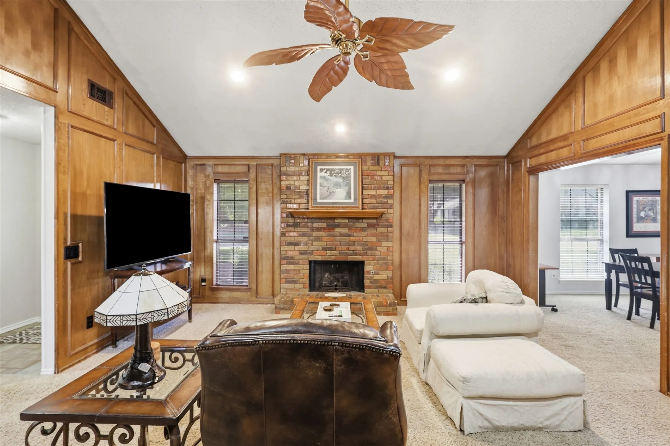 Living space featuring extensive wood paneling, a brick fireplace with a wood mantle, and a vaulted ceiling with a ceiling fan