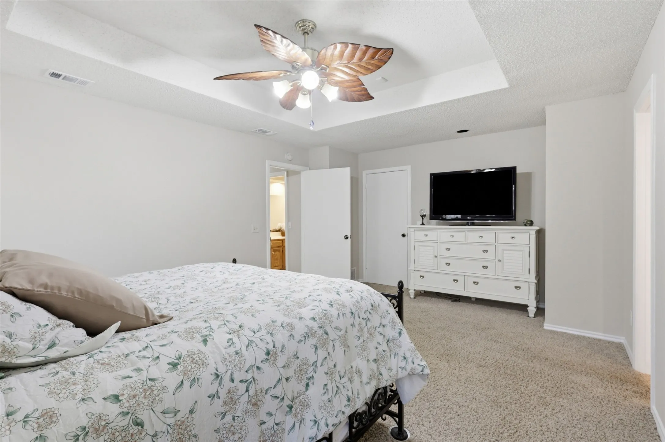Bedroom featuring a tray ceiling, ceiling fan with light fixture, and neutral carpeting