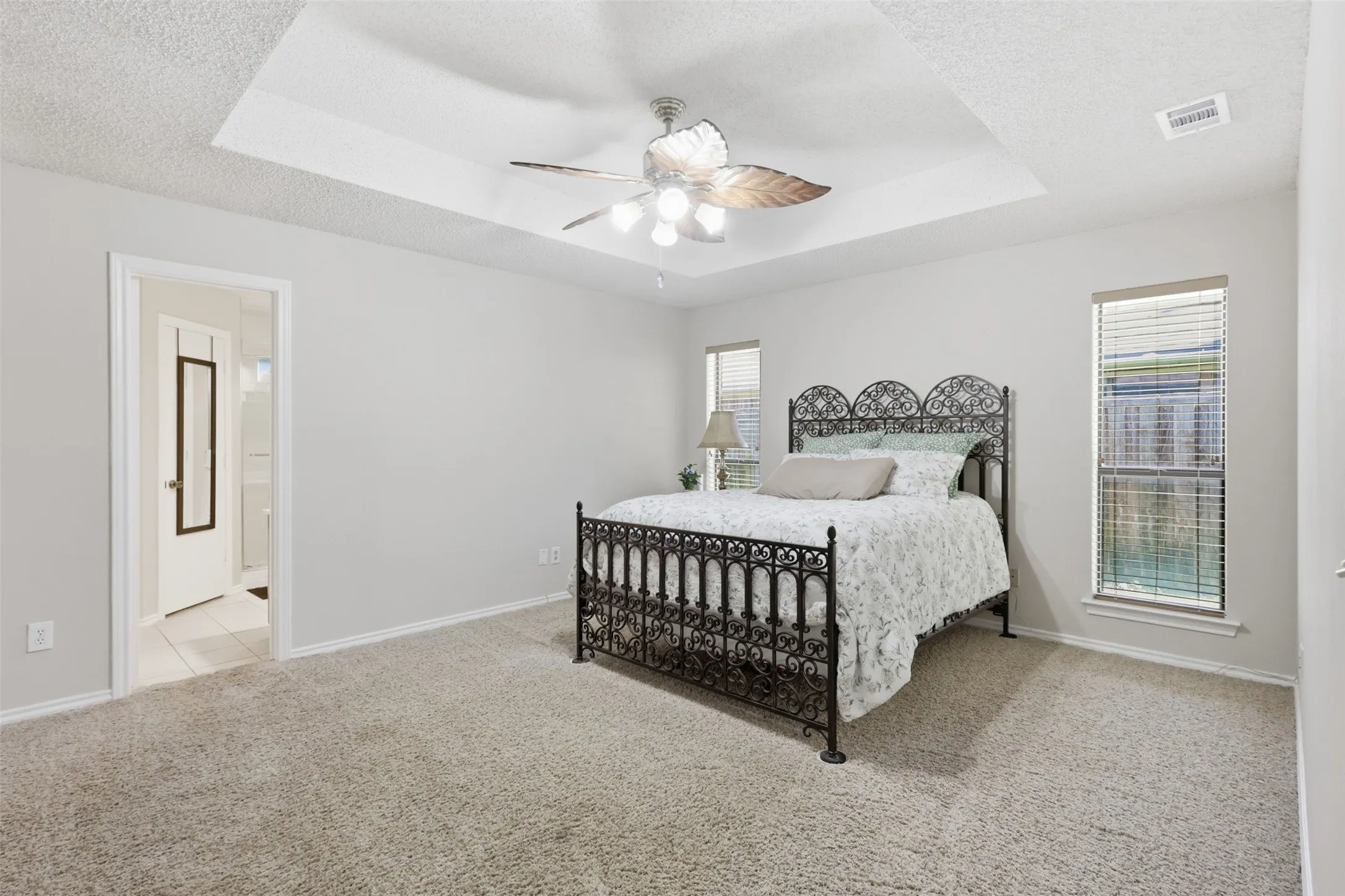 Spacious room featuring a tray ceiling with a ceiling fan, neutral carpeting, and two windows with blinds
