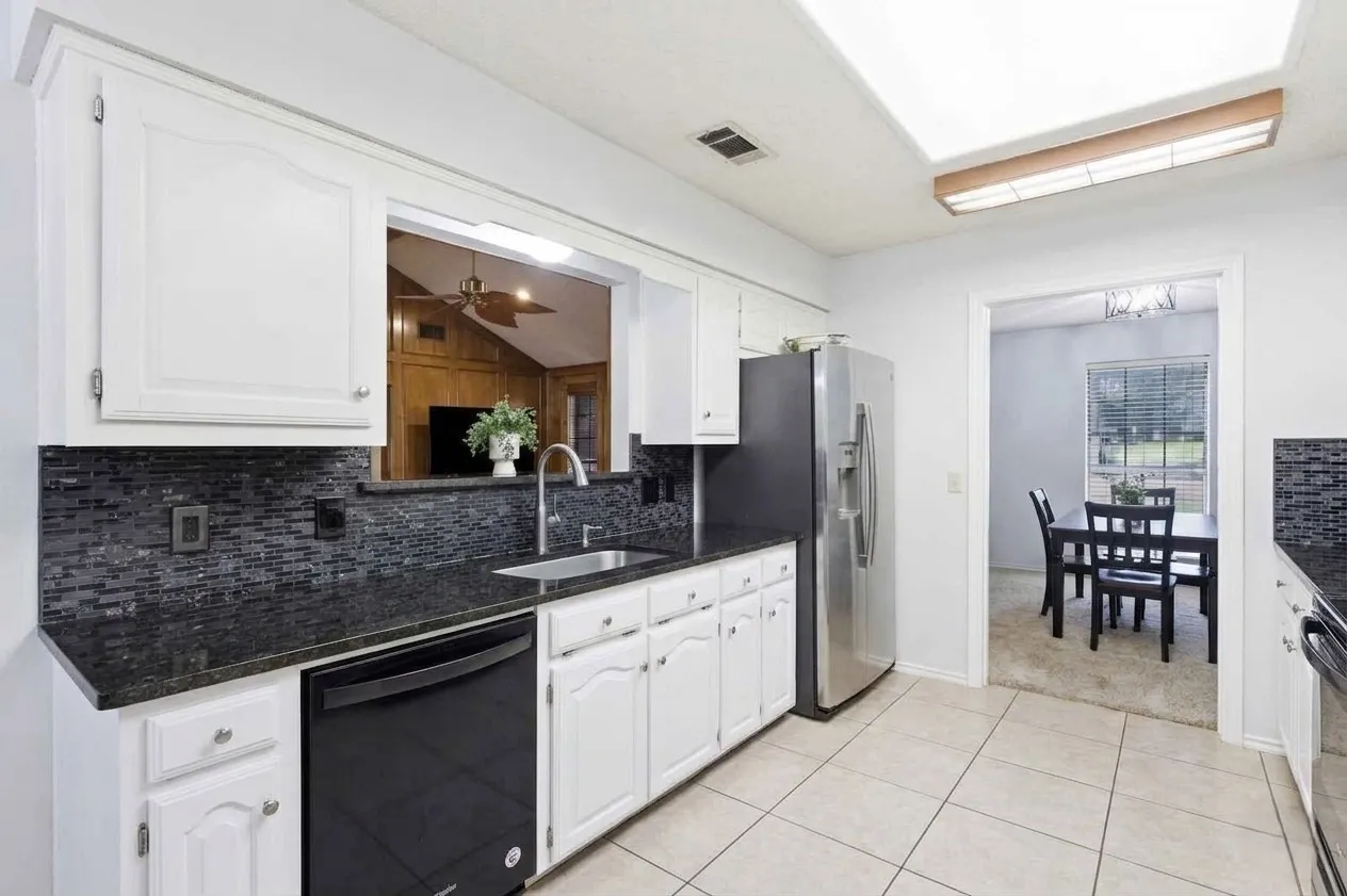 Kitchen featuring white cabinetry, black stone countertops, mosaic tile backsplash, and tile flooring