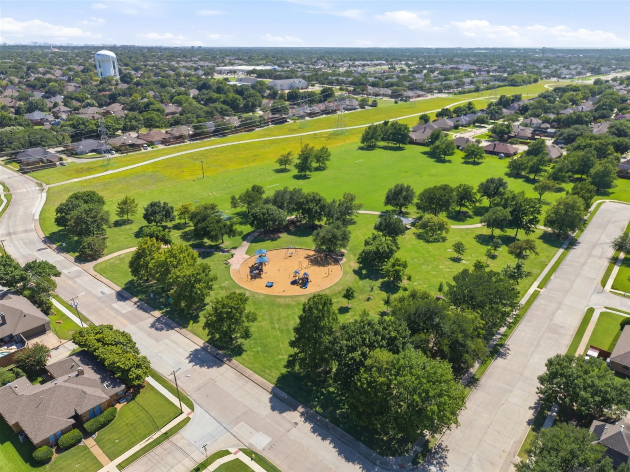 Expansive community park featuring a playground, mature trees, and a walking path surrounded by residential properties