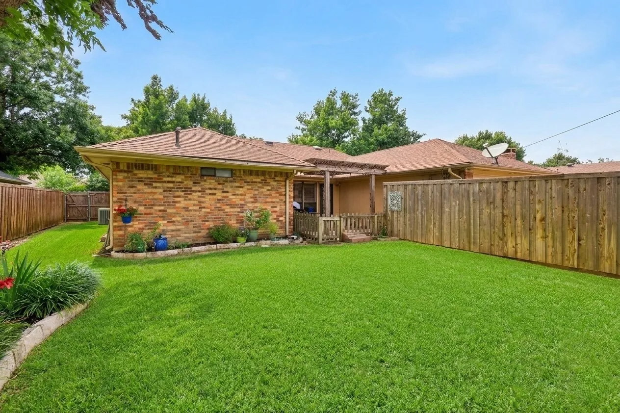 Expansive backyard featuring a lush lawn, solid wood privacy fencing, and brick exterior
