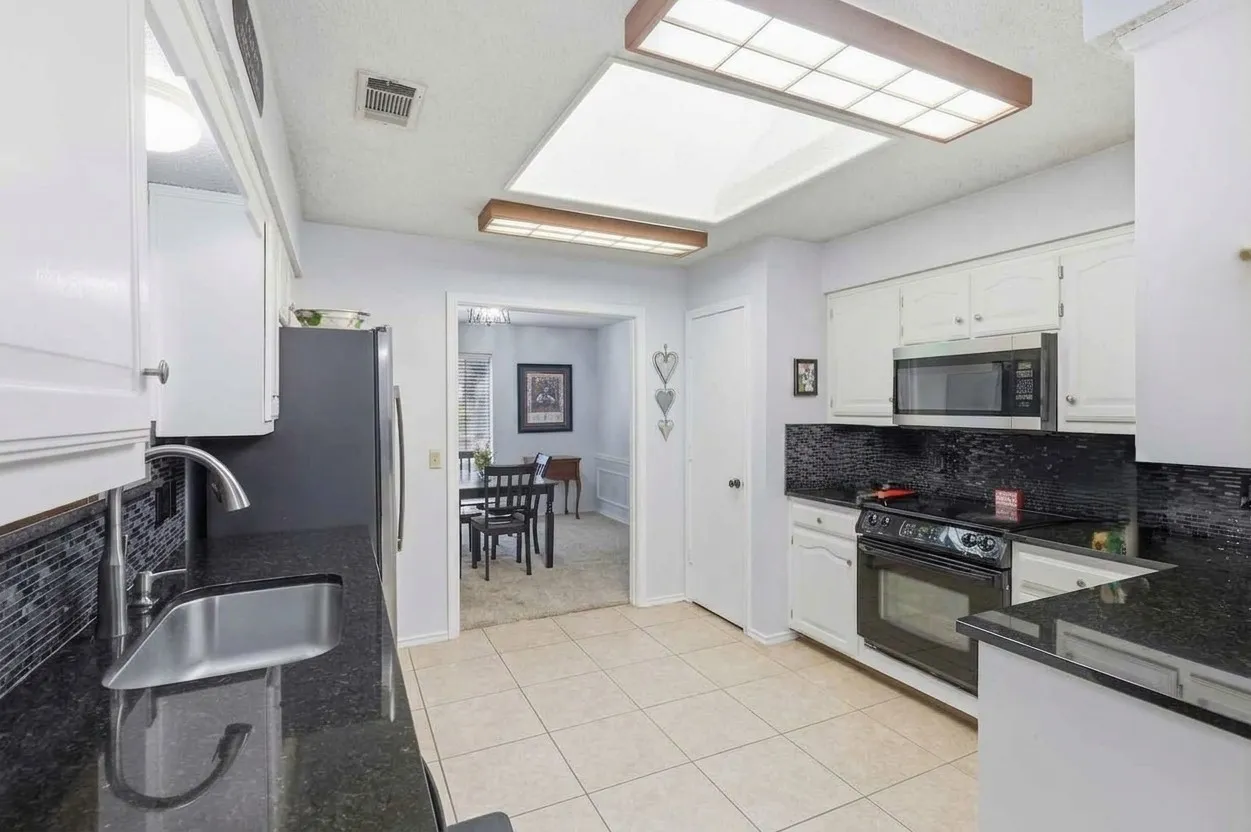 Kitchen featuring white cabinetry, black granite-style countertops, mosaic tile backsplash, and stainless steel appliances