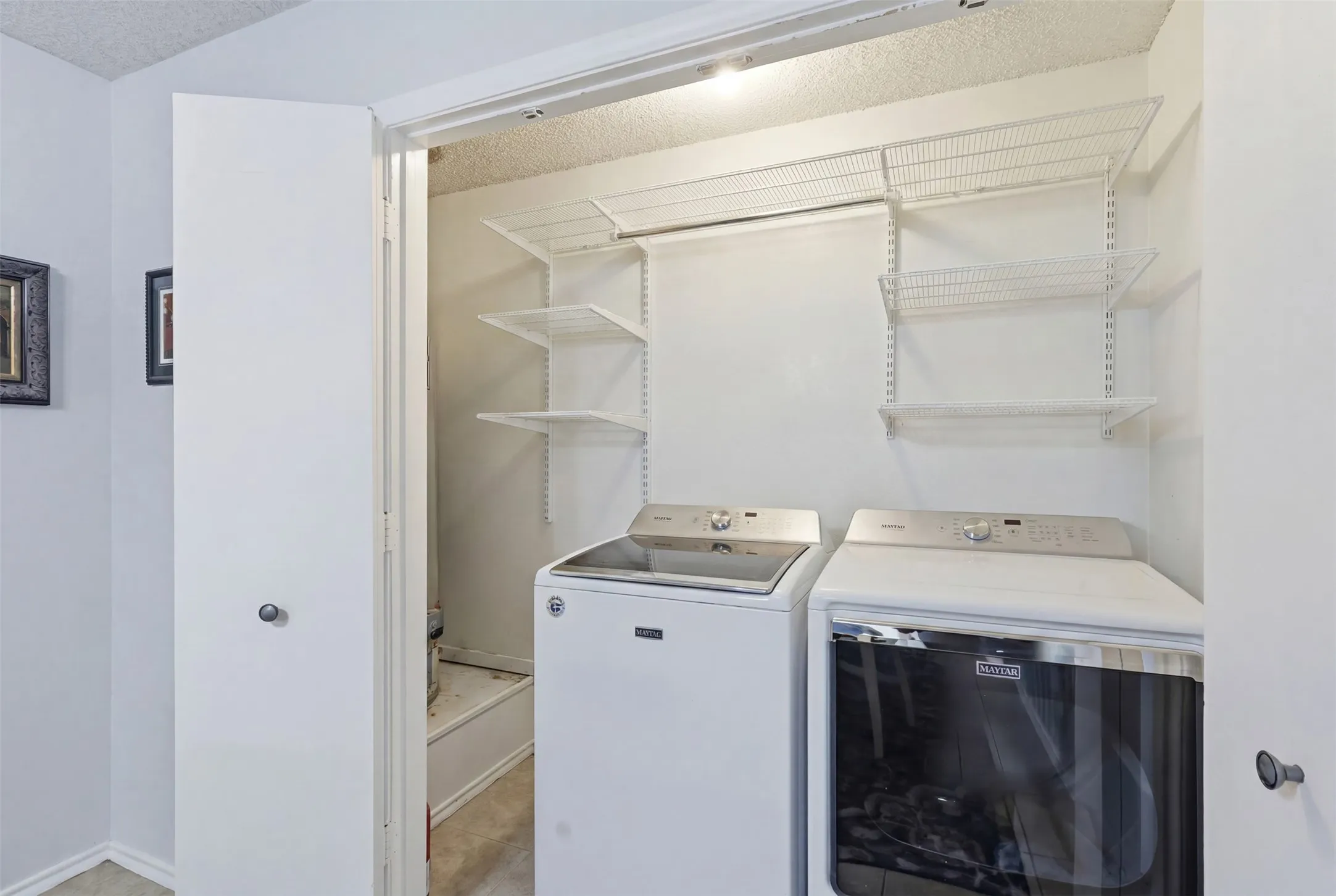 Dedicated laundry closet featuring top-loading machines, built-in wire shelving, and overhead lighting