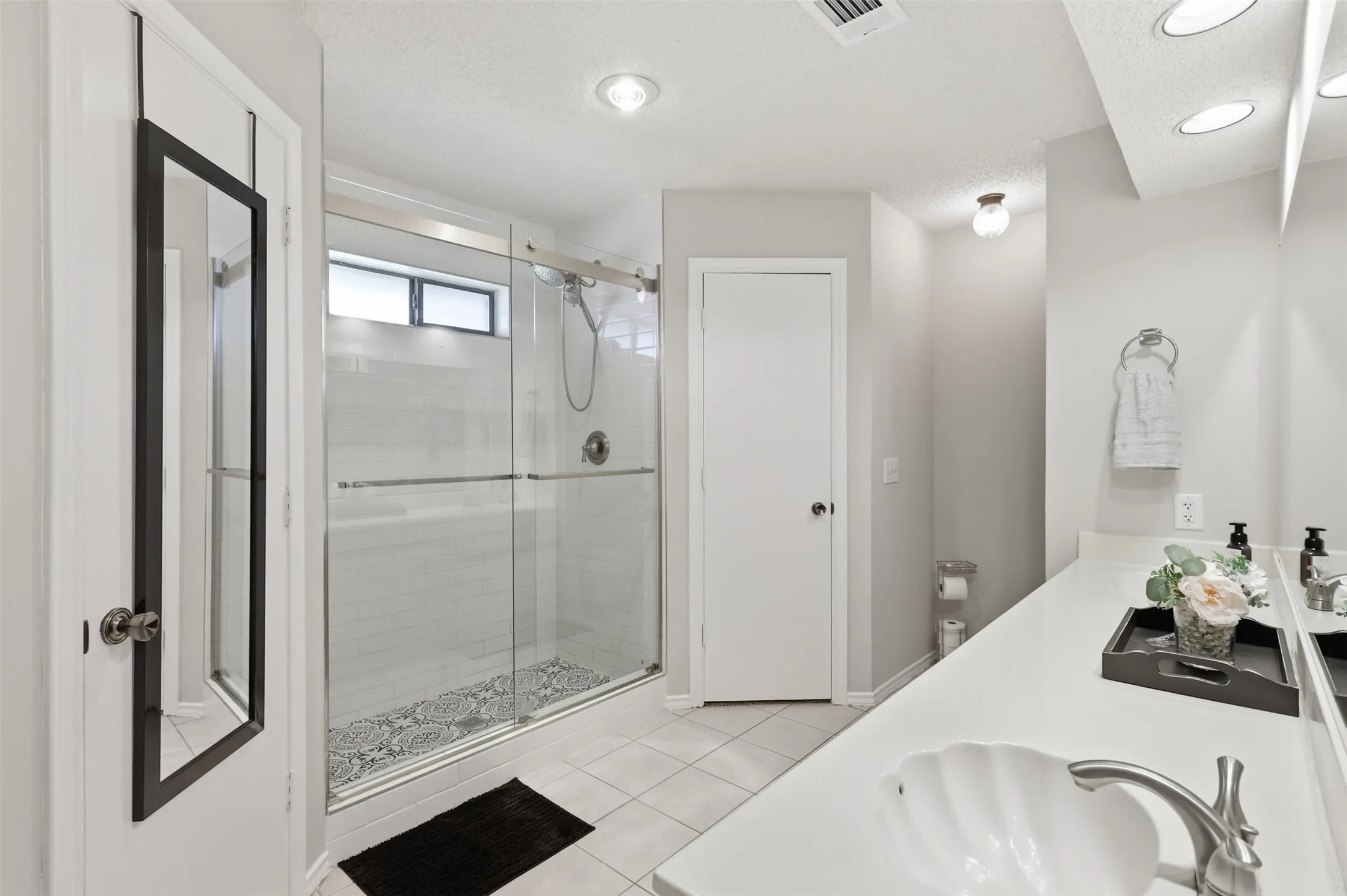 Bathroom featuring a glass-enclosed shower with tile surround, a built-in vanity with a shell-shaped basin, a chrome faucet, recessed ceiling lighting, and tile flooring