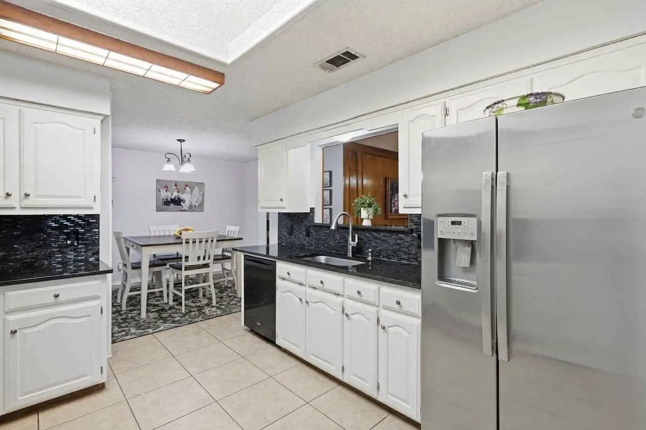 Kitchen featuring white cabinetry, black countertops, a mosaic tile backsplash, stainless steel refrigerator, and tile flooring