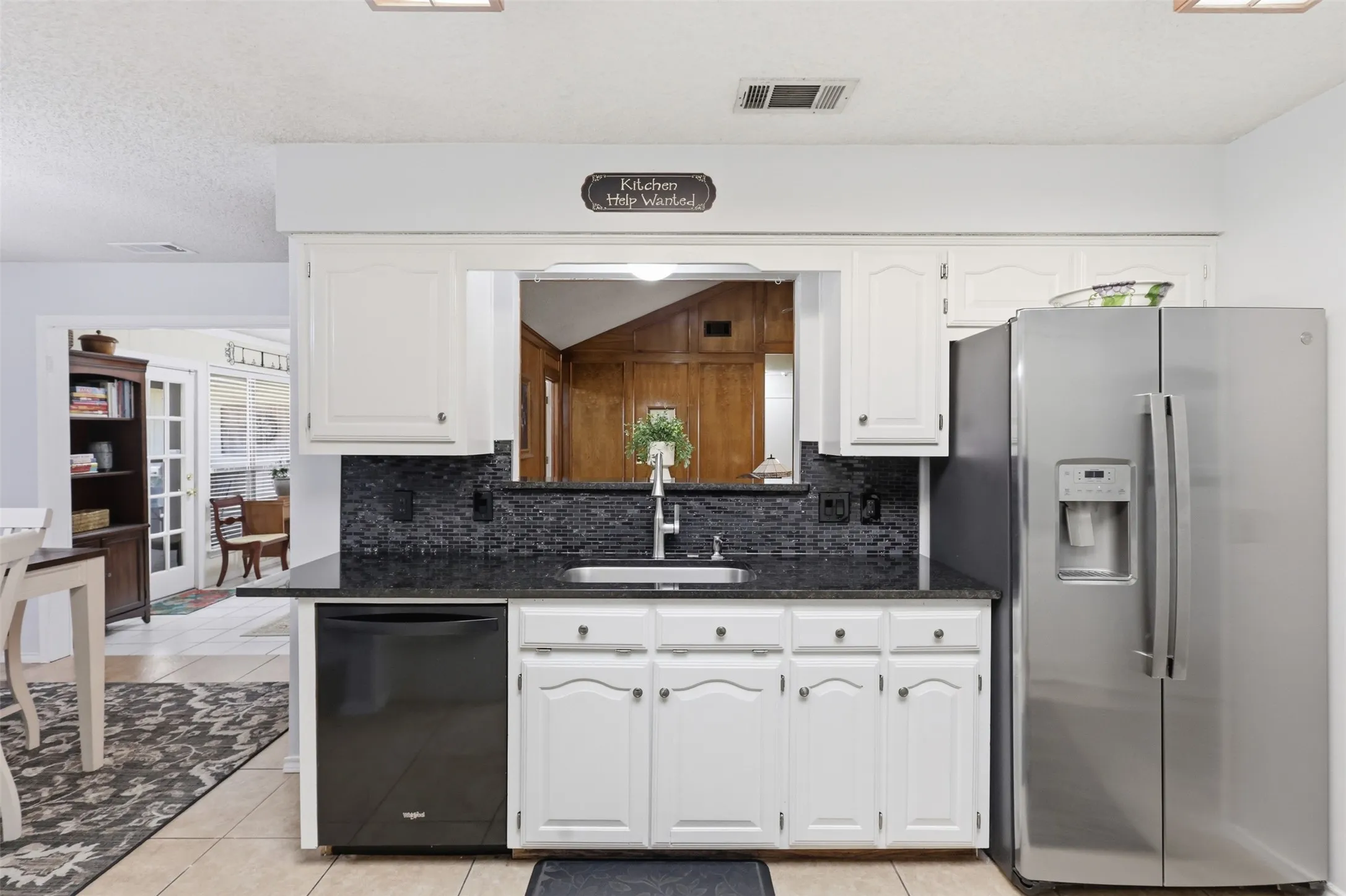Kitchen featuring white cabinetry, dark countertop, black tile backsplash, stainless steel refrigerator, and integrated dishwasher