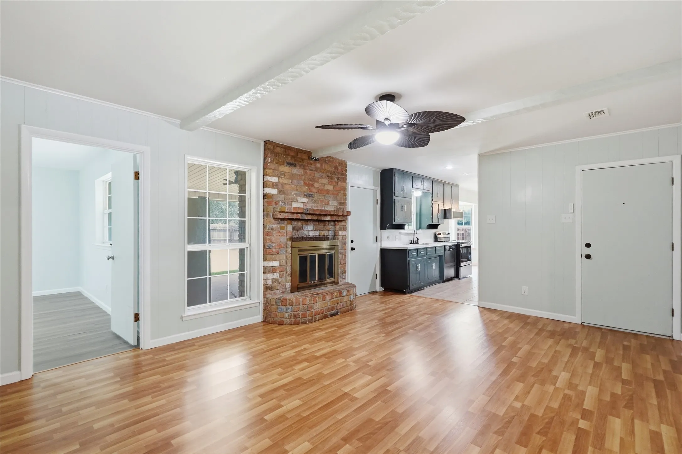 Spacious living area featuring wood-finish flooring, a brick fireplace with a metal insert, and a ceiling fan