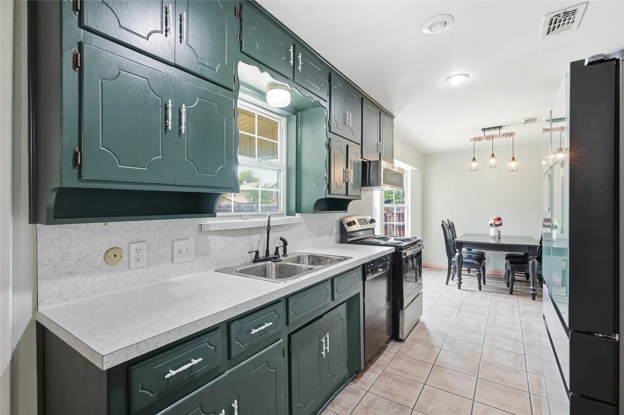 Kitchen featuring teal cabinetry with decorative paneling and silver-tone hardware, white speckled countertops, and a double basin sink with a black faucet