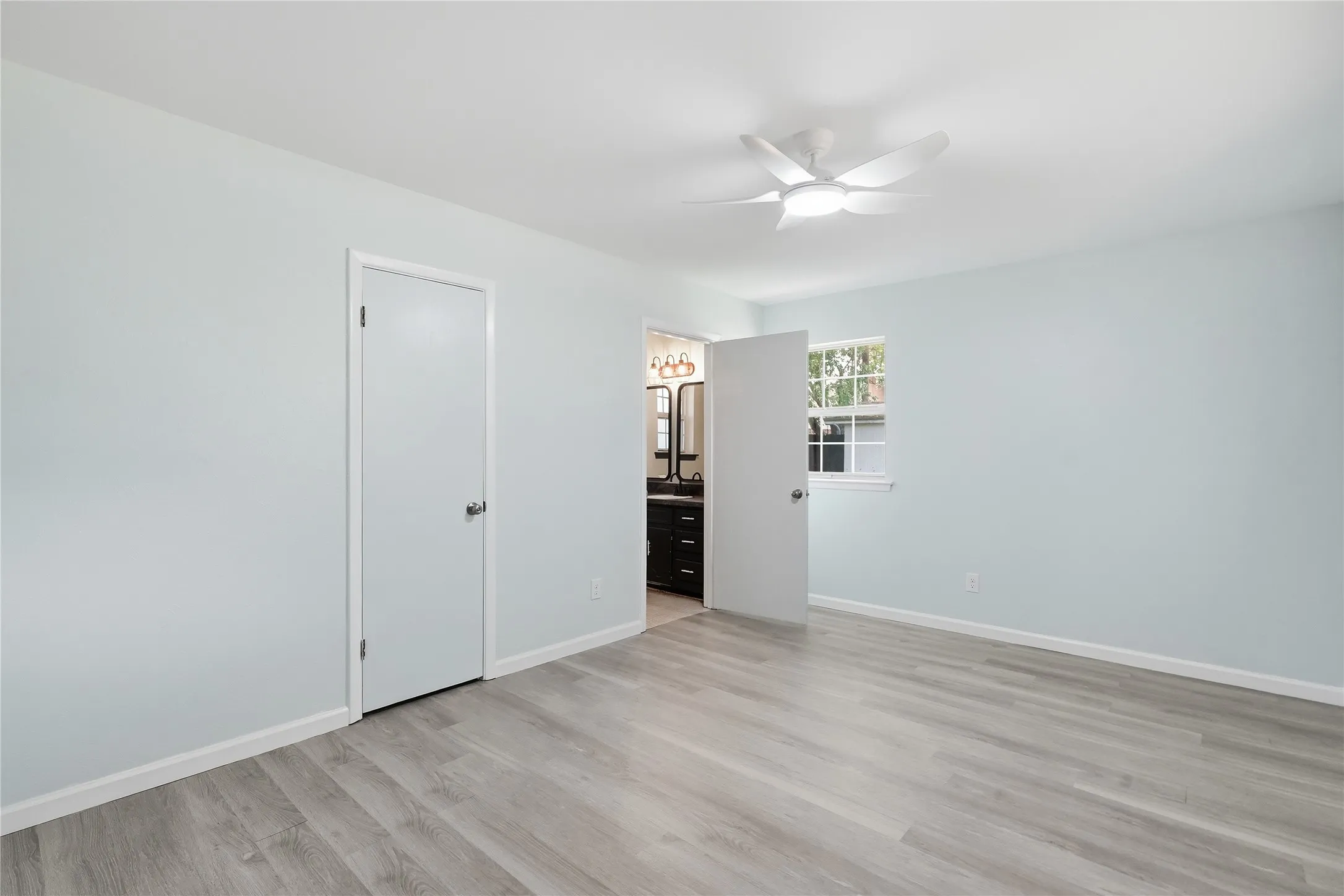Spacious room featuring wood-finish flooring, light blue walls, and a white ceiling fan