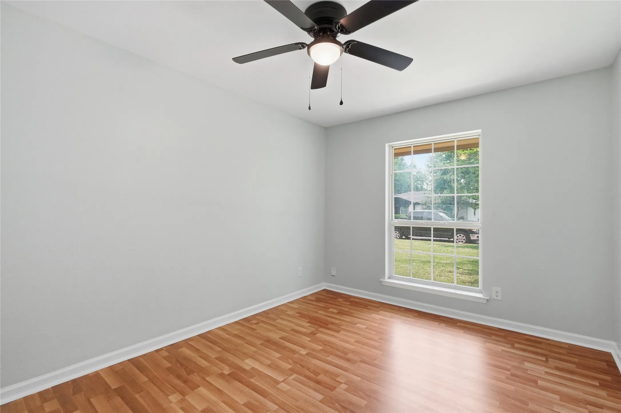 Light-filled interior space featuring wood-finish flooring, a contemporary ceiling fan with integrated lighting, and a multi-pane window