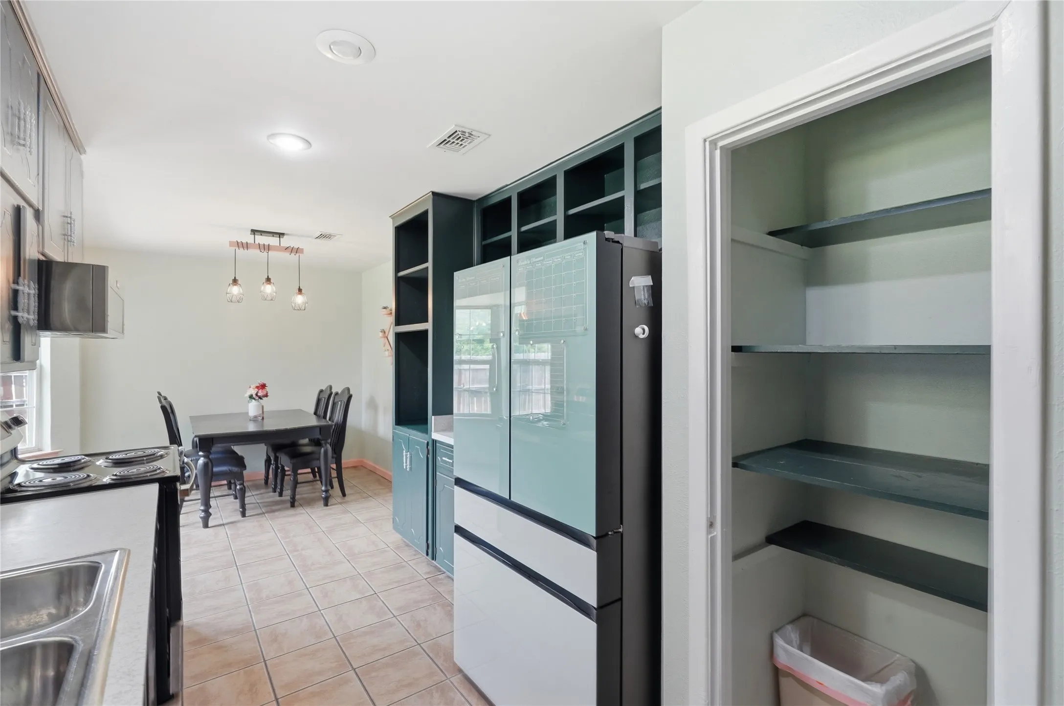 Kitchen and dining area featuring tile flooring, recessed lighting, built-in shelving, a kitchen sink with a stainless steel faucet, and a contemporary linear pendant light fixture