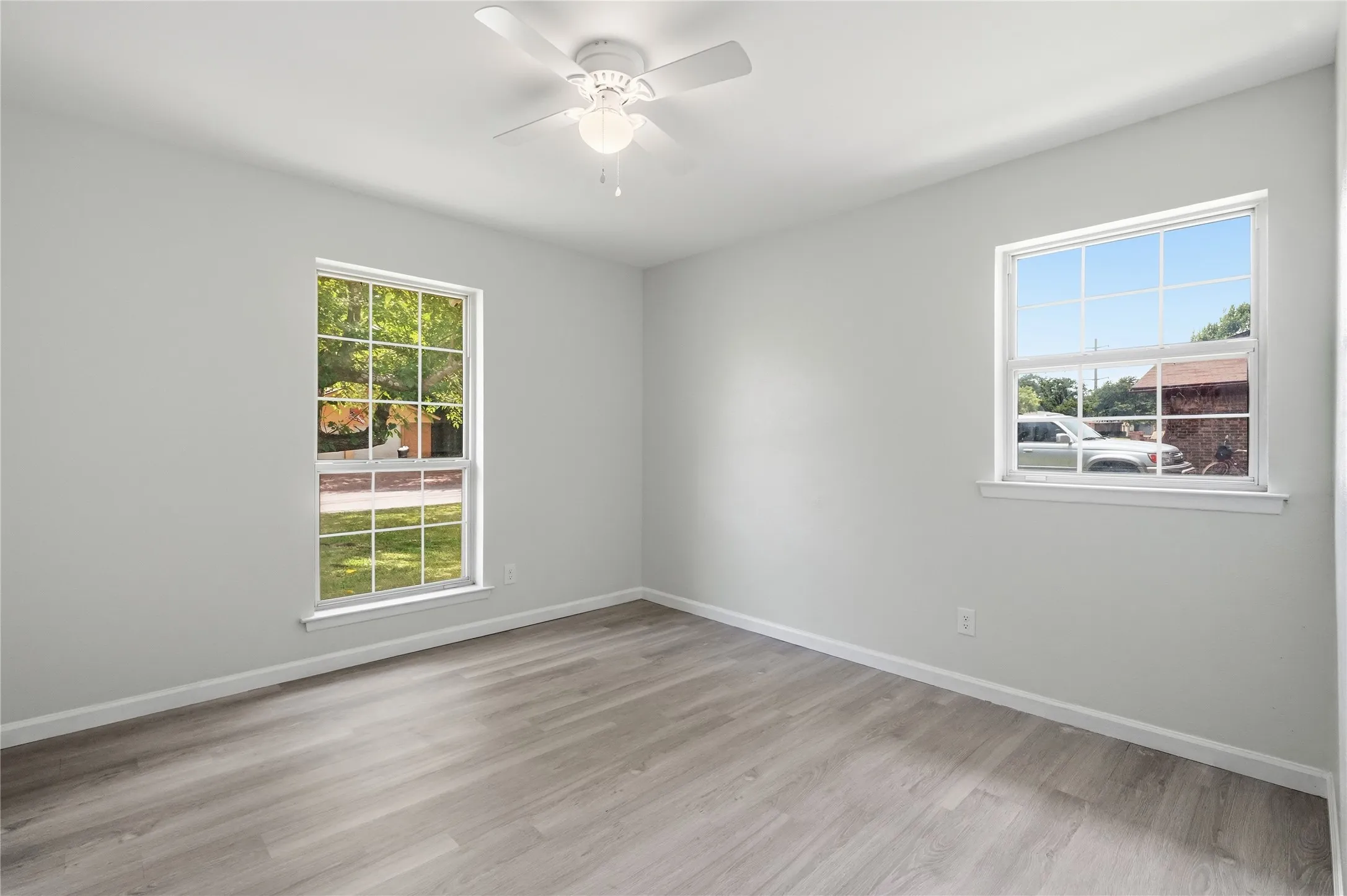 Spacious room featuring light gray walls, wood-finish flooring, and multiple windows with white trim