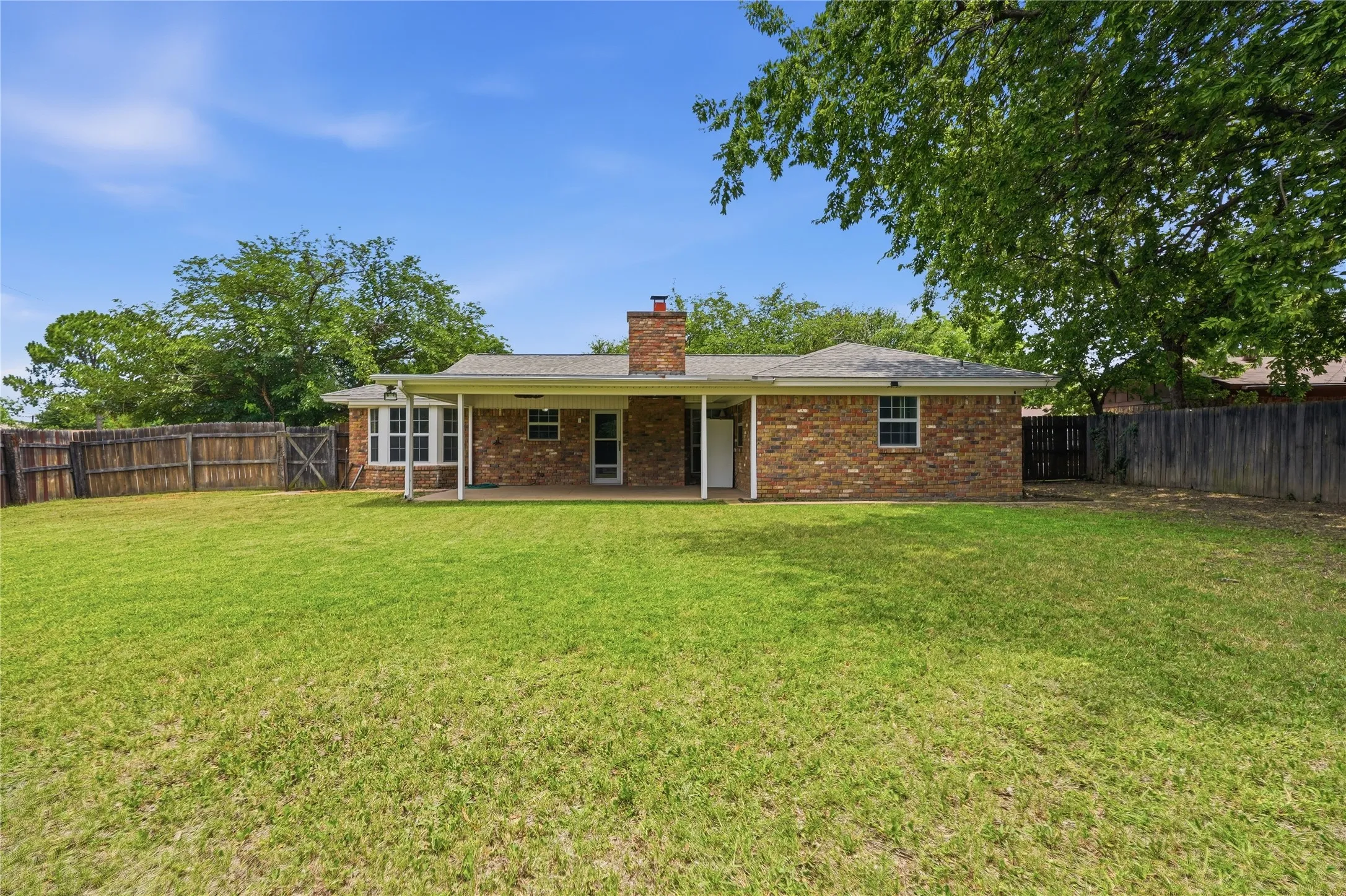Expansive lawn featuring a privacy fence and mature trees