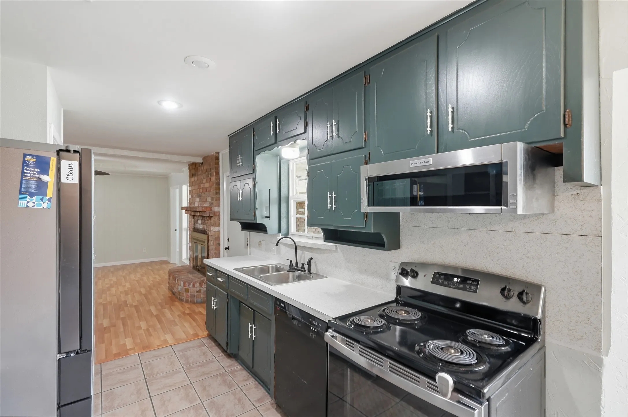 Kitchen featuring dark teal cabinetry, stainless steel appliances including a refrigerator, range, and built-in microwave, white countertops, and a double basin sink with a gooseneck faucet