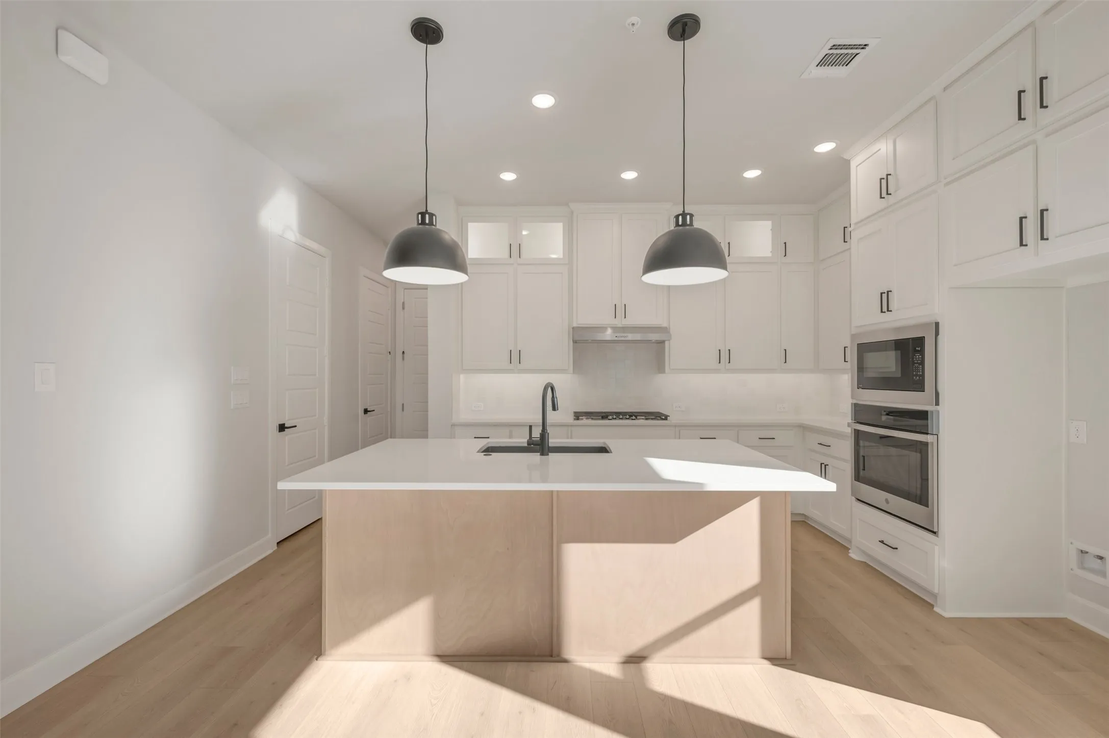 Gourmet kitchen featuring a central island with a sink, stainless steel appliances, white cabinetry, and wood-finish flooring