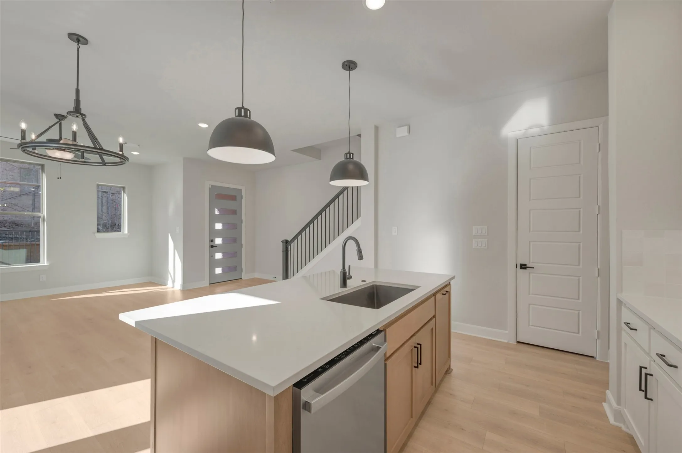 Kitchen island with an undermount sink and white countertop, light wood-finish flooring, metal spindle staircase, and a paneled entry door