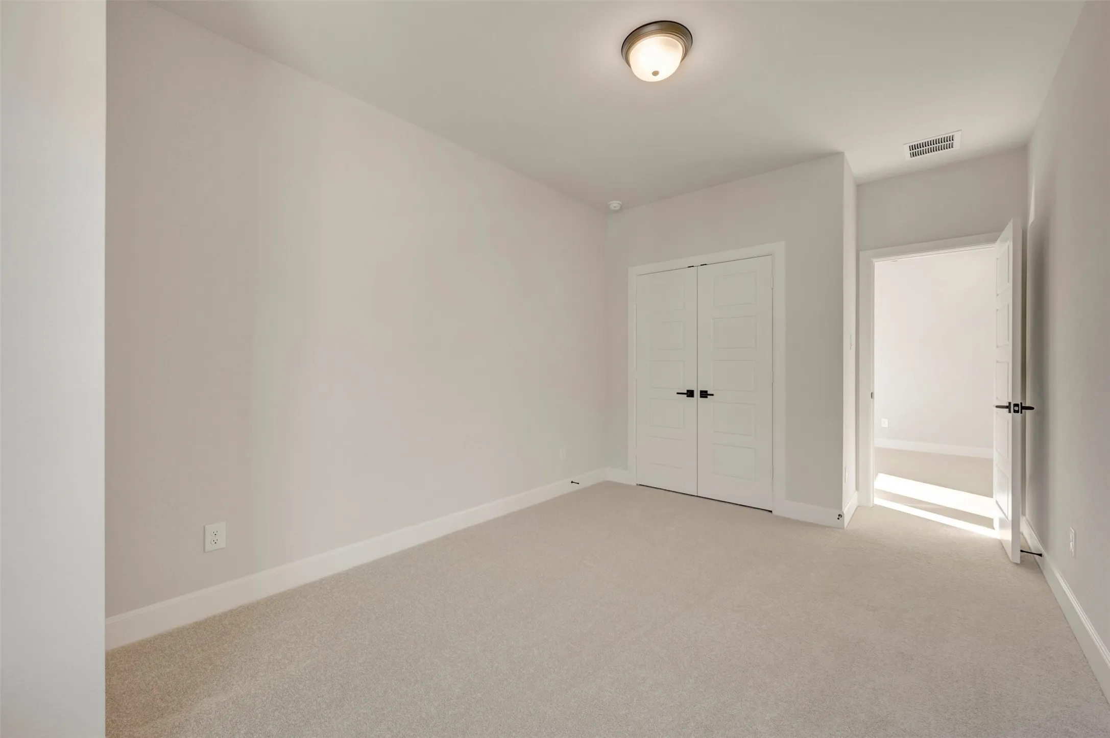 Light-toned walls, neutral carpet flooring, double panel doors with black hardware, and a semi-flush mount ceiling light