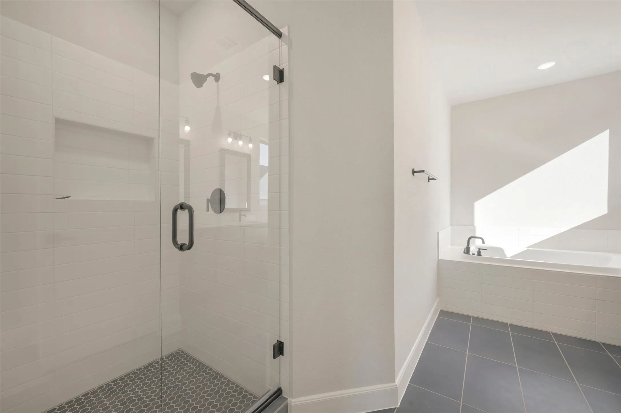 Glass-enclosed shower with subway tile surround and hexagonal mosaic tile floor, featuring matte black fixtures