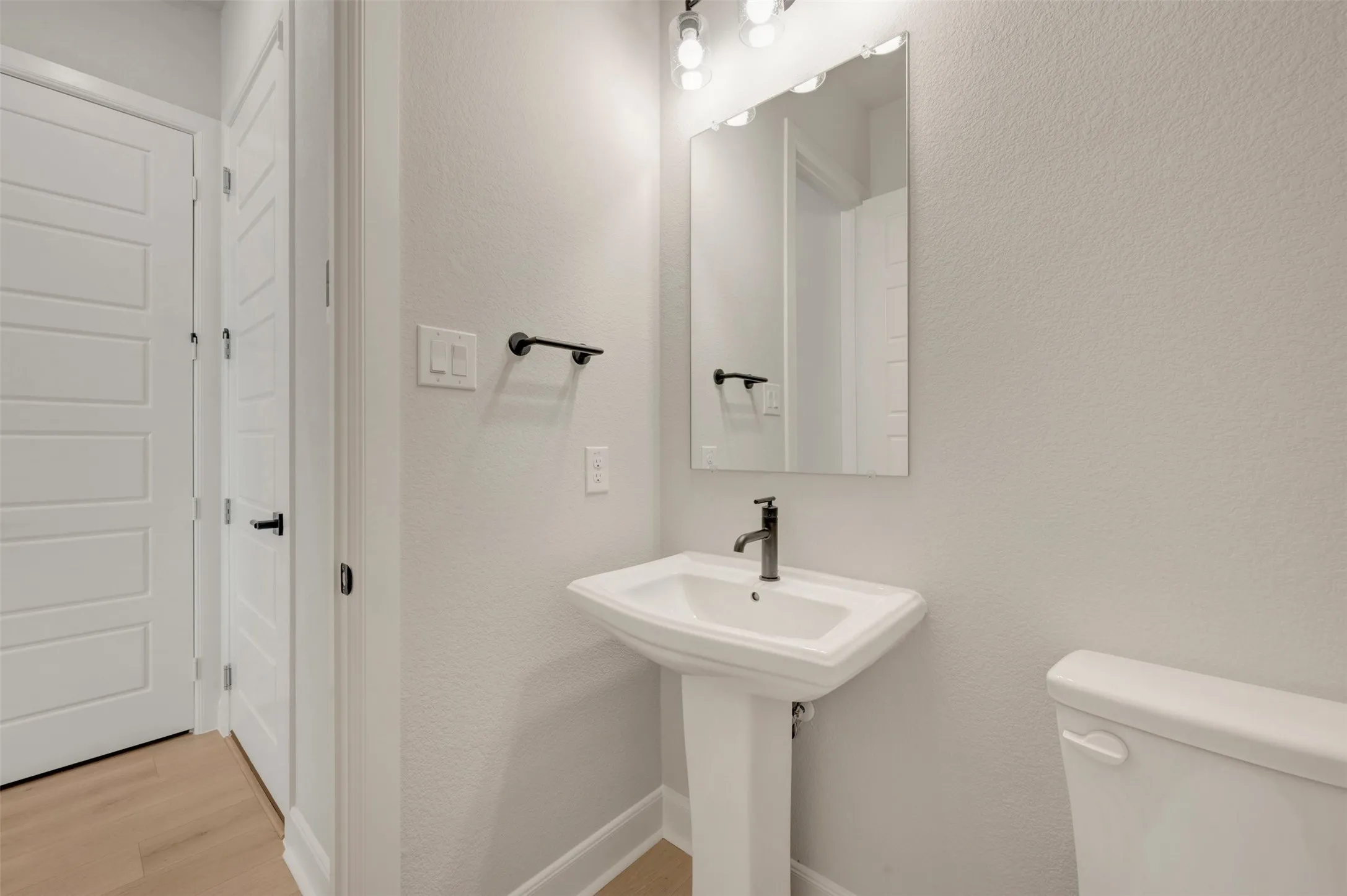 Pedestal sink with a matte black faucet, rectangular mirror, and overhead vanity lighting