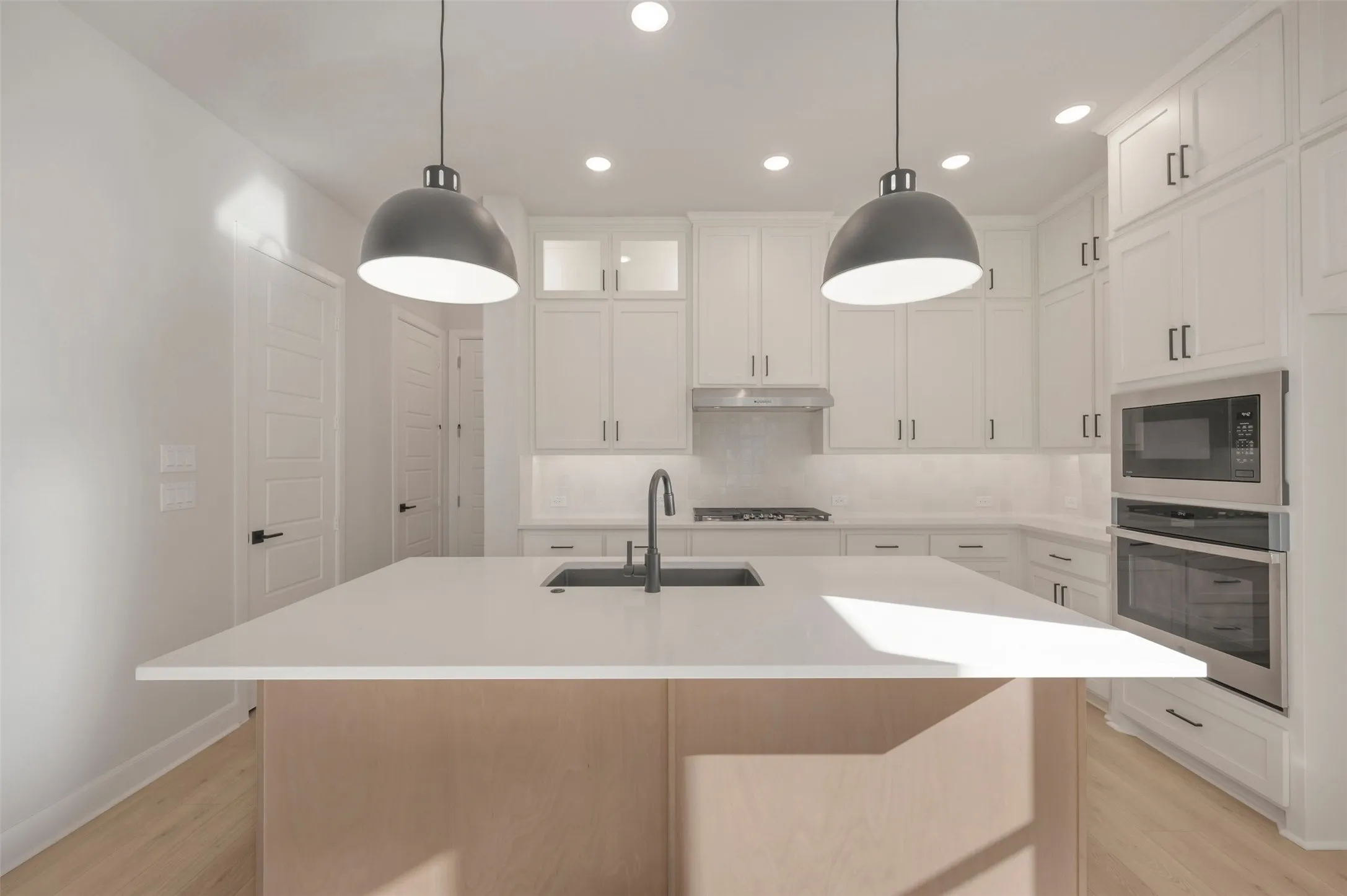 Kitchen featuring a large central island, white cabinetry with dark hardware, stainless steel appliances, and two pendant lights