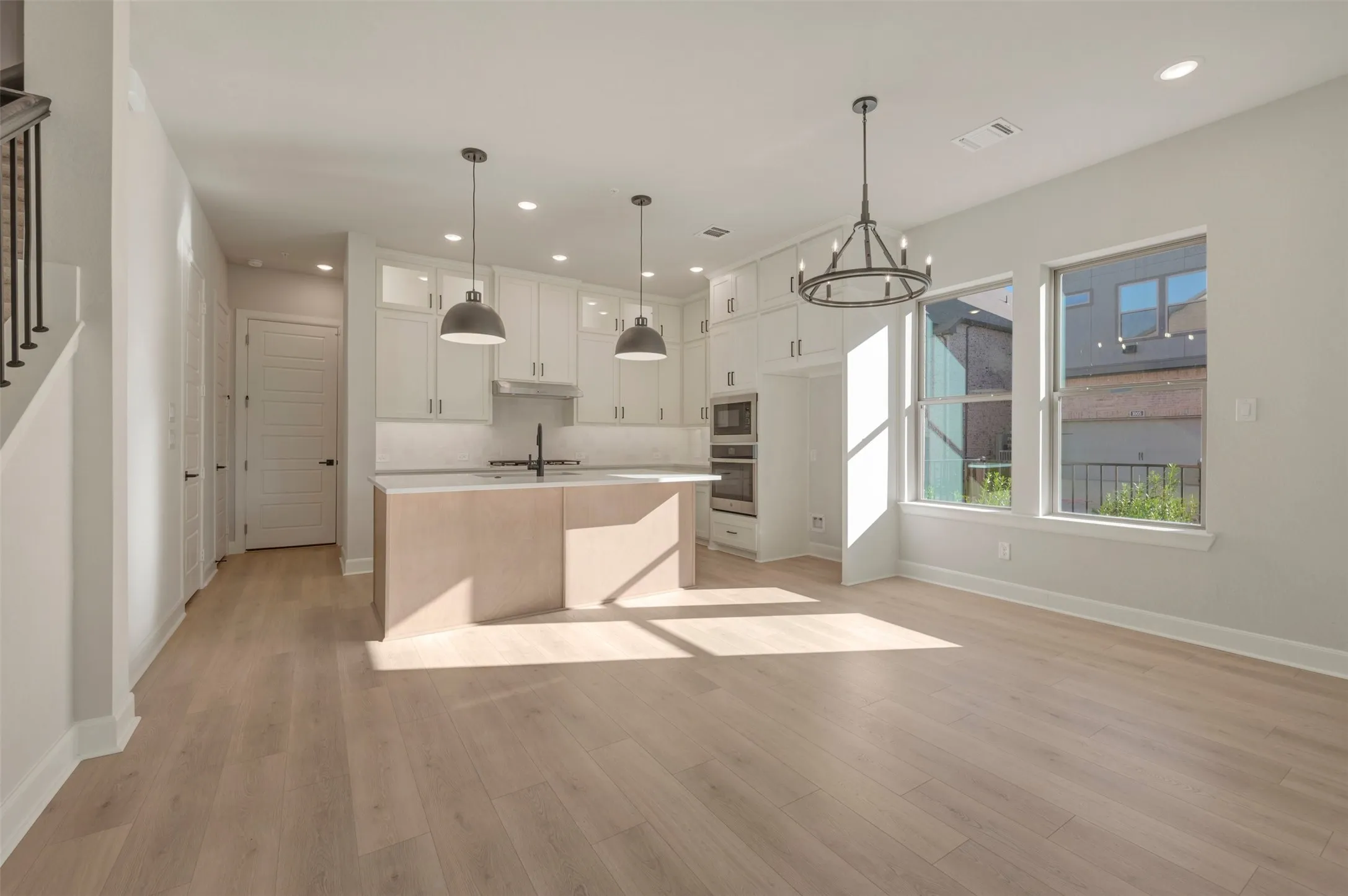 Open-concept living space with light wood-finish flooring, white shaker cabinetry, stainless steel appliances, and a kitchen island with pendant lighting