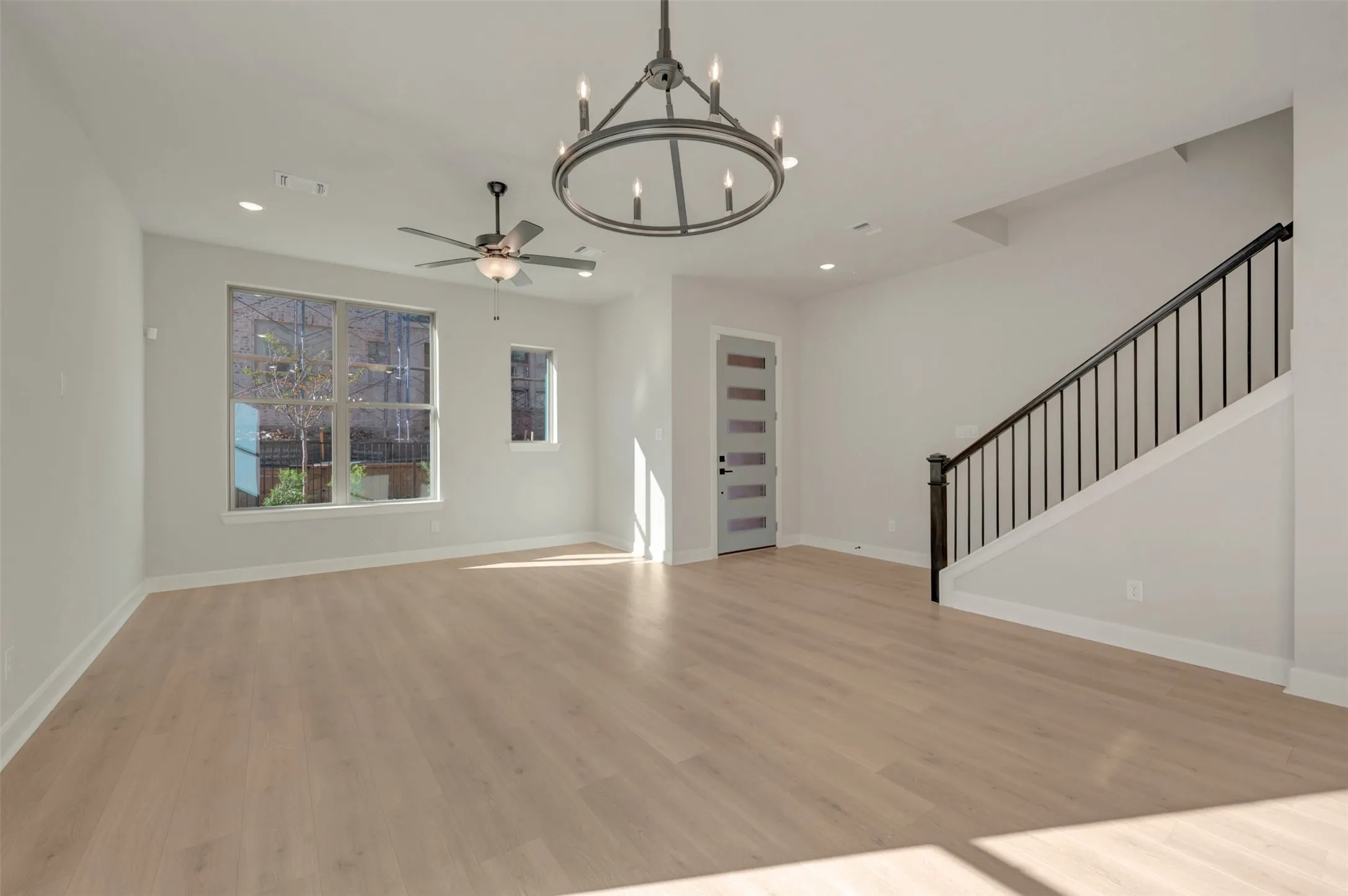 Spacious interior featuring wood-finish flooring, a contemporary chandelier, a ceiling fan, and a modern entrance door with frosted glass panels