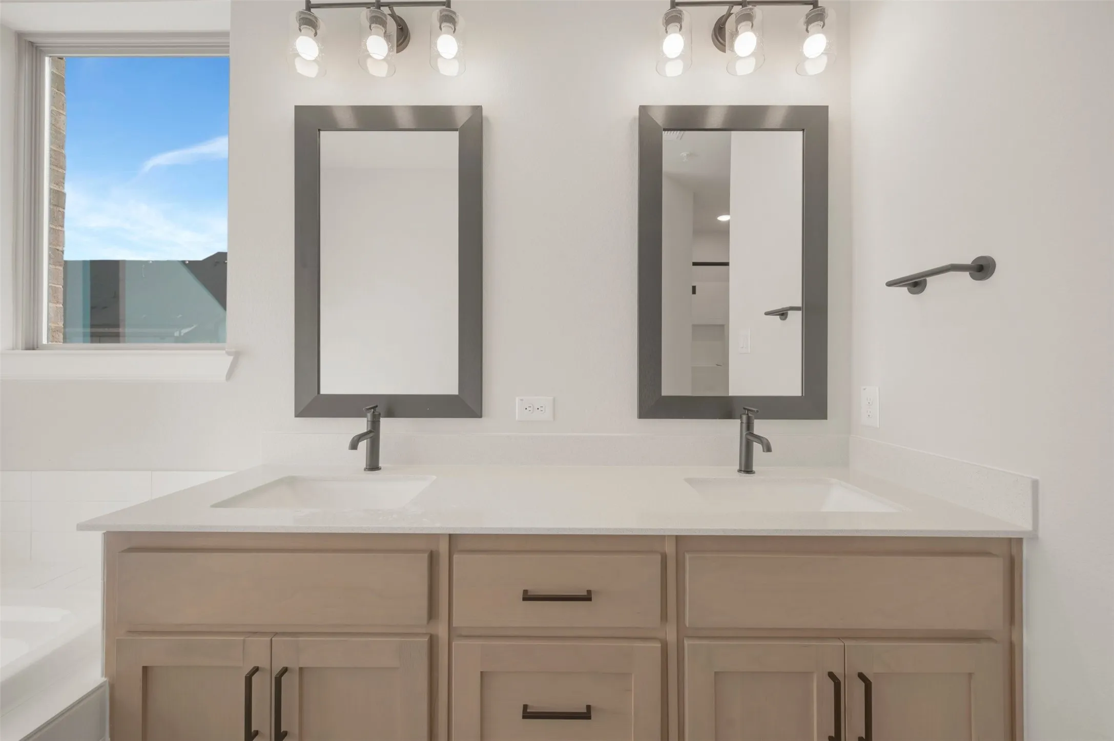 Dual vanity with light wood-finish cabinetry, integrated sinks, and matte black fixtures