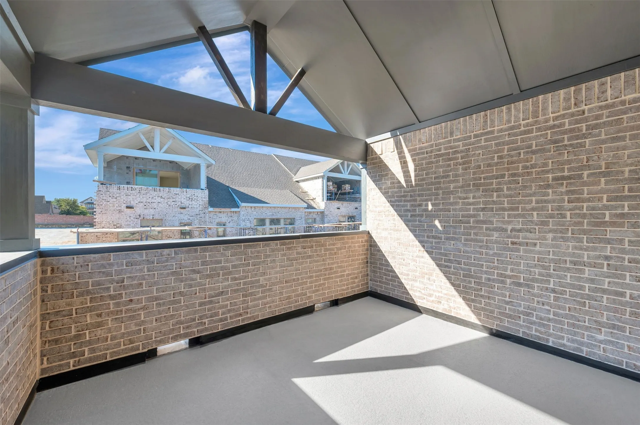 Covered outdoor entertaining space featuring exposed beam ceiling detail, expansive brick walls, polished concrete flooring, and abundant natural light from clerestory windows