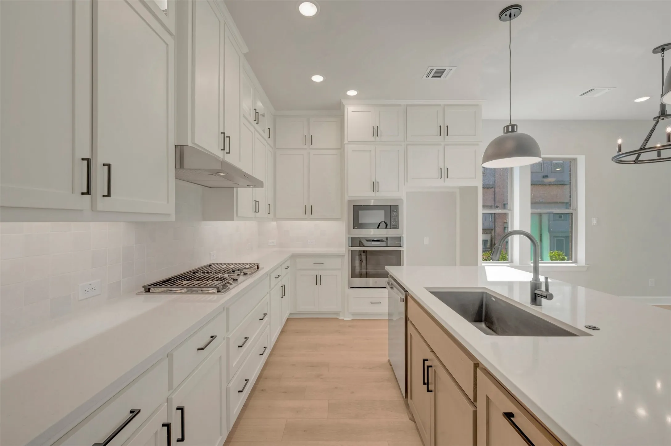 White shaker-style cabinetry with black hardware, white countertops, built-in stainless steel appliances, and a kitchen island with an undermount sink